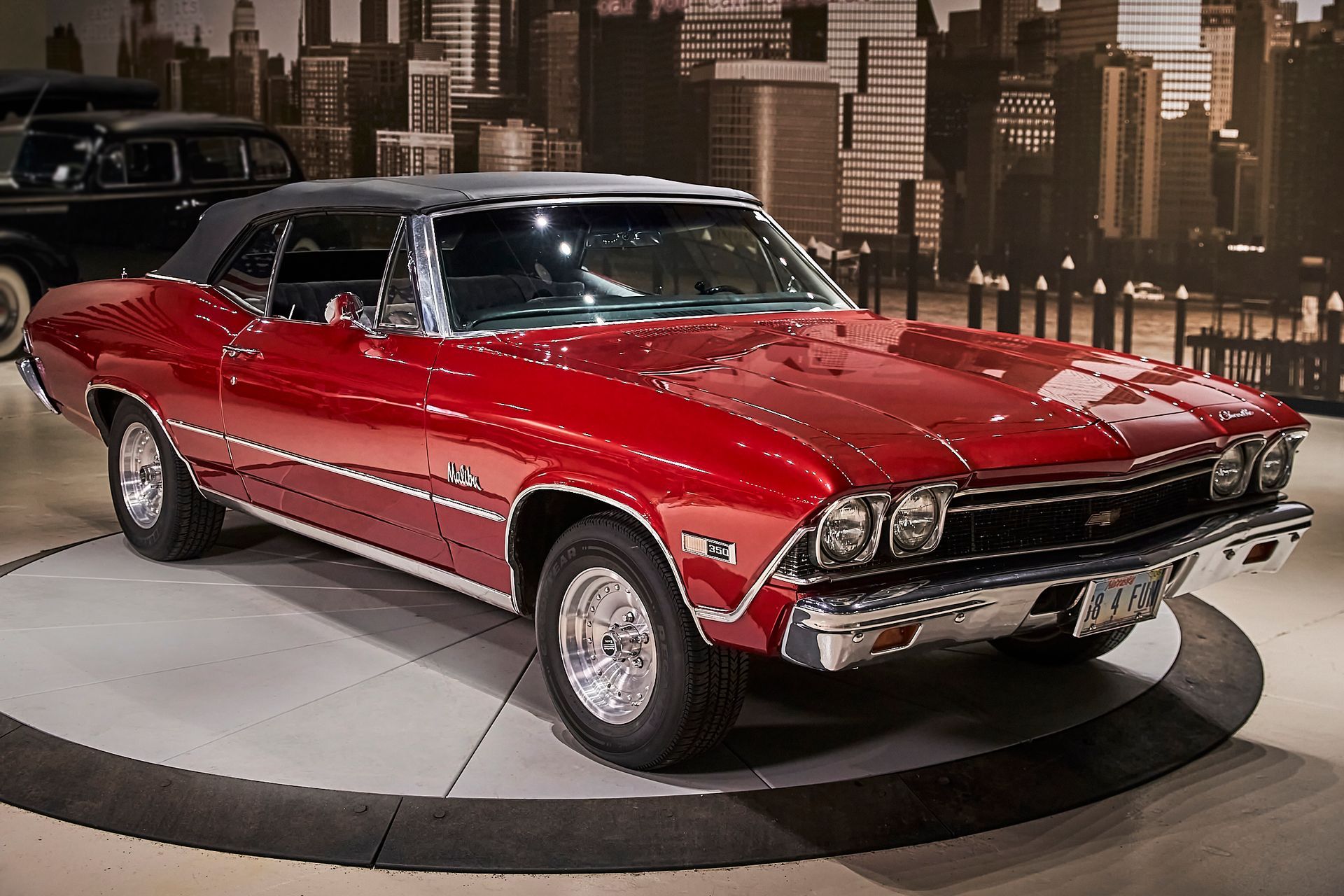 A red car is parked in front of a city skyline
