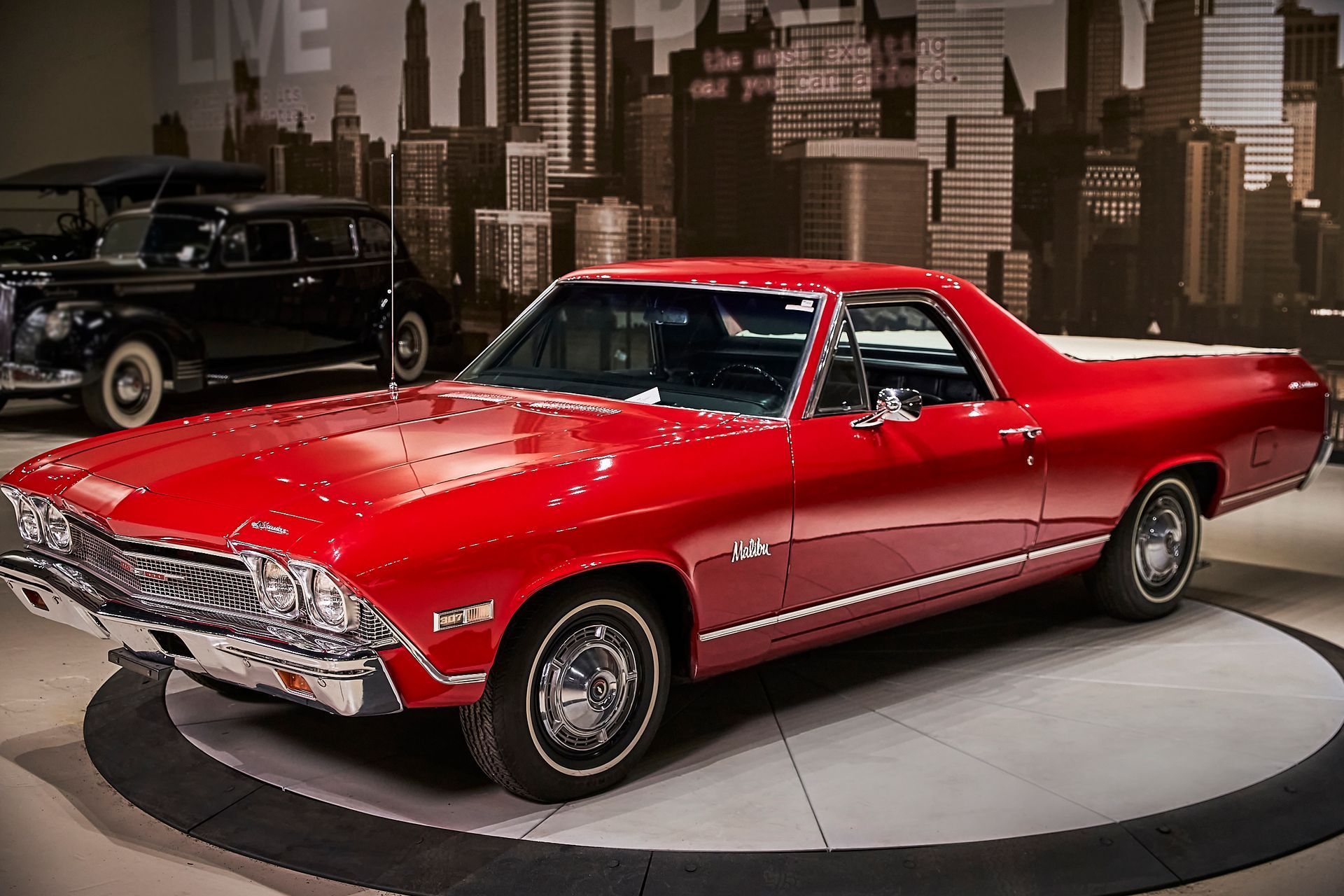 A red car is parked in front of a city skyline