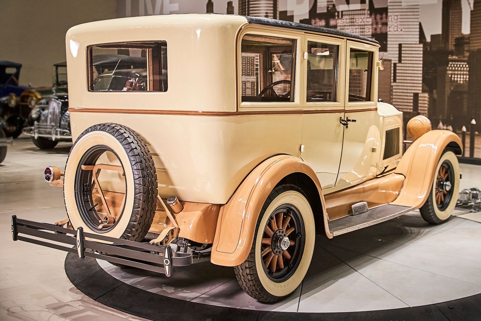 An old fashioned car is parked in a garage with a city in the background