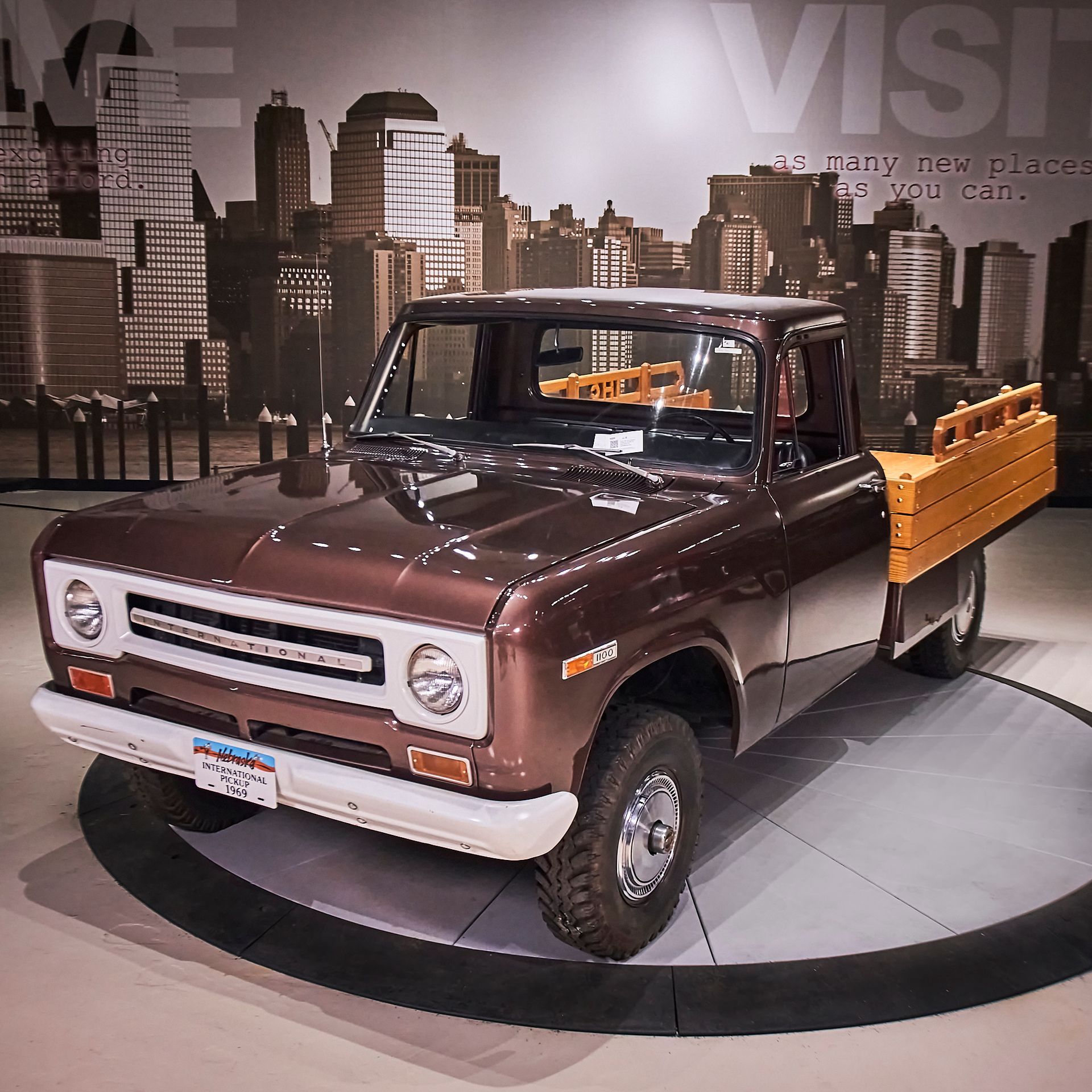 A brown truck is on display in front of a sign that says visit