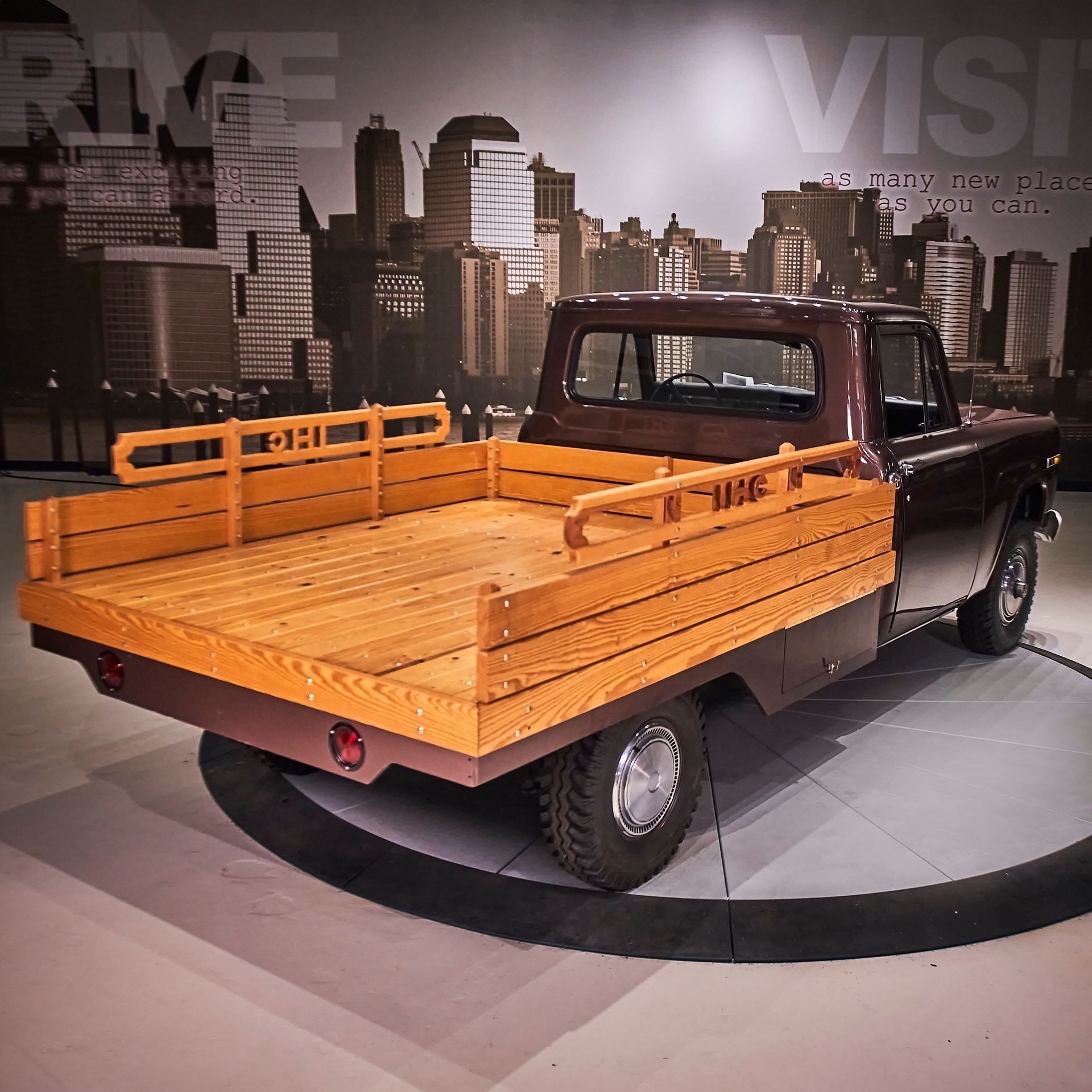 A brown truck with a wooden bed is parked in front of a city skyline