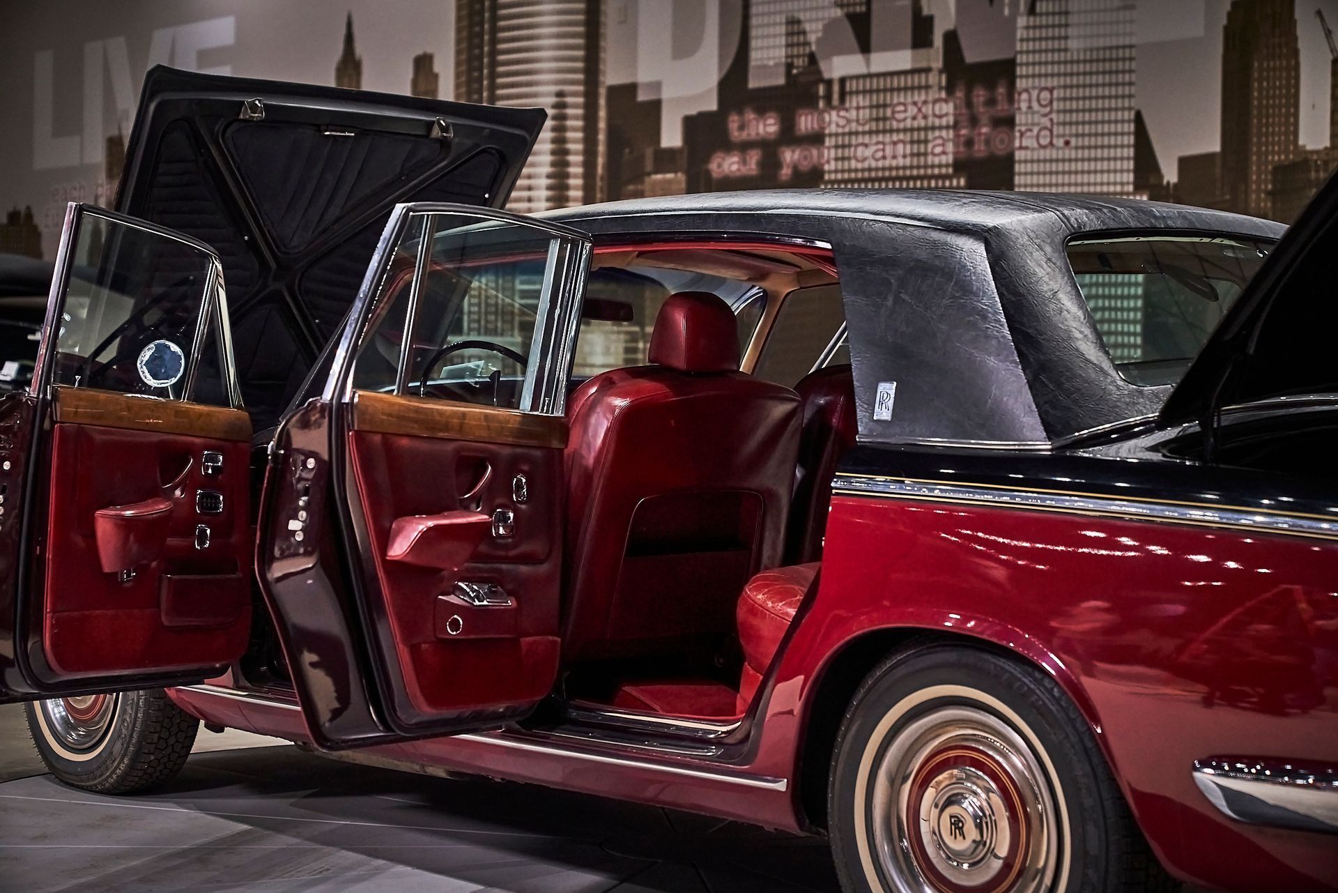 A red car with its doors open is parked in front of a city skyline.
