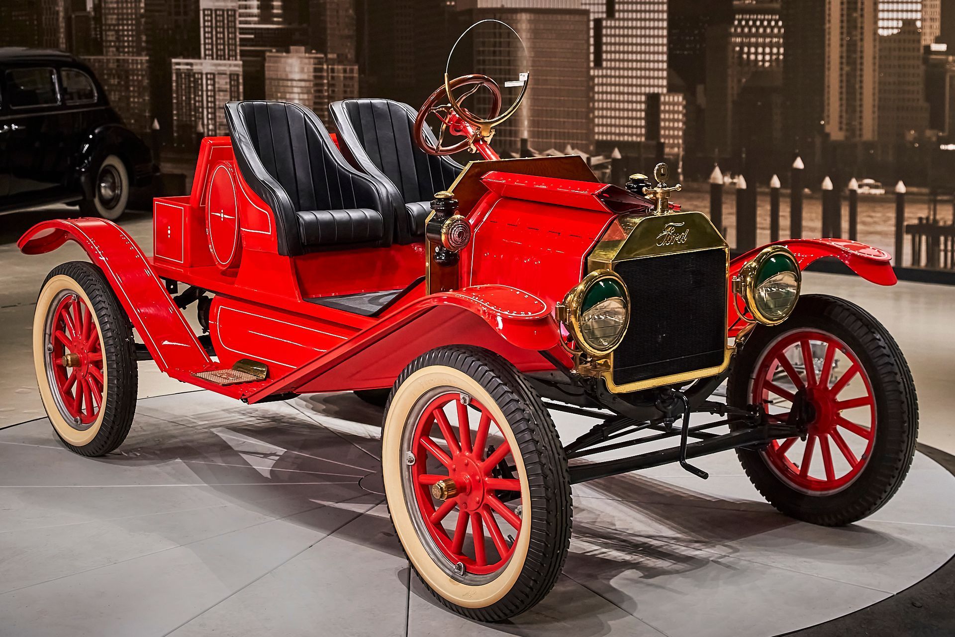 An old red car with white tires is parked in a garage.