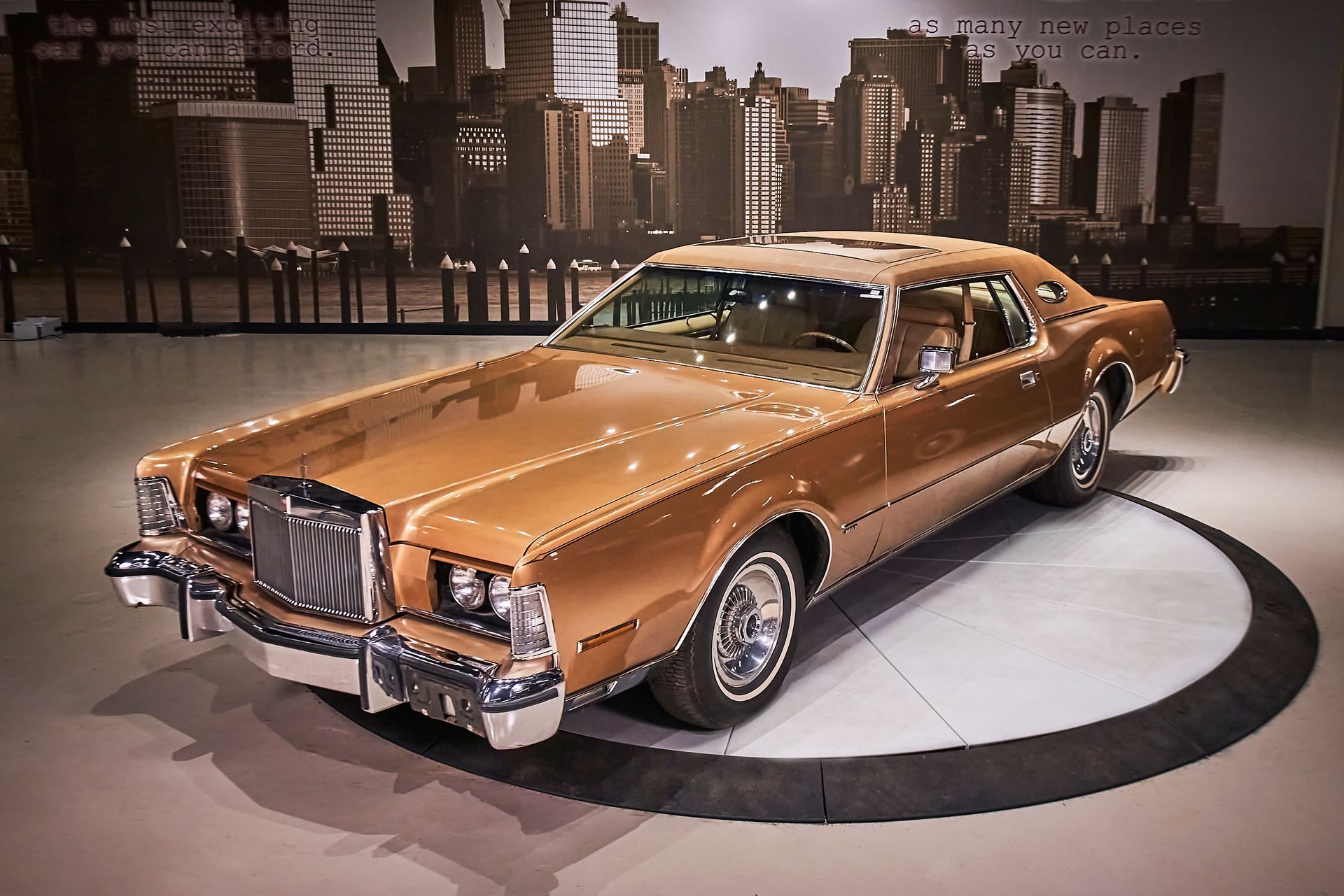 A gold car is parked in front of a city skyline
