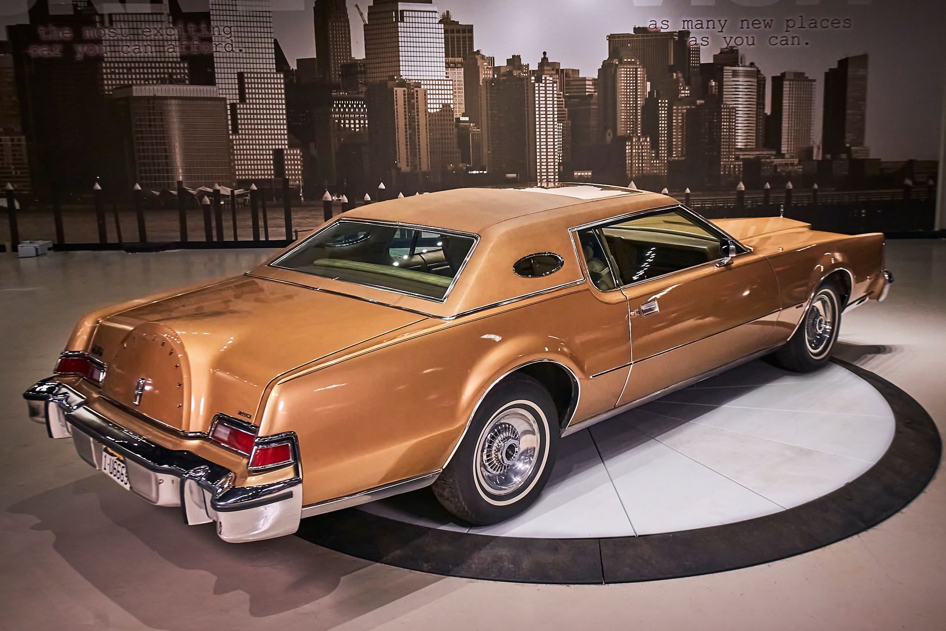 A gold car is parked in front of a city skyline