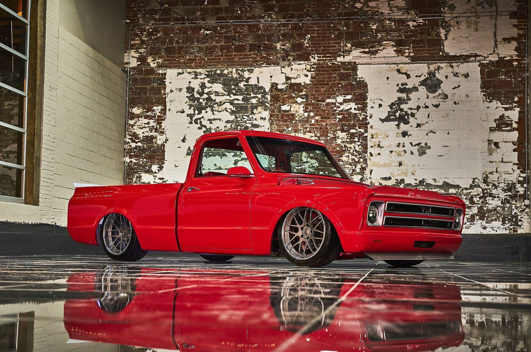 A red truck is parked in front of a brick wall in a garage.