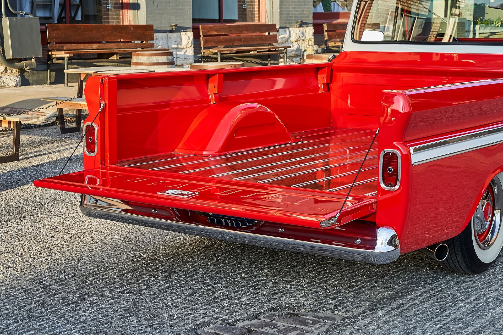 A red truck with the back door open is parked on gravel.