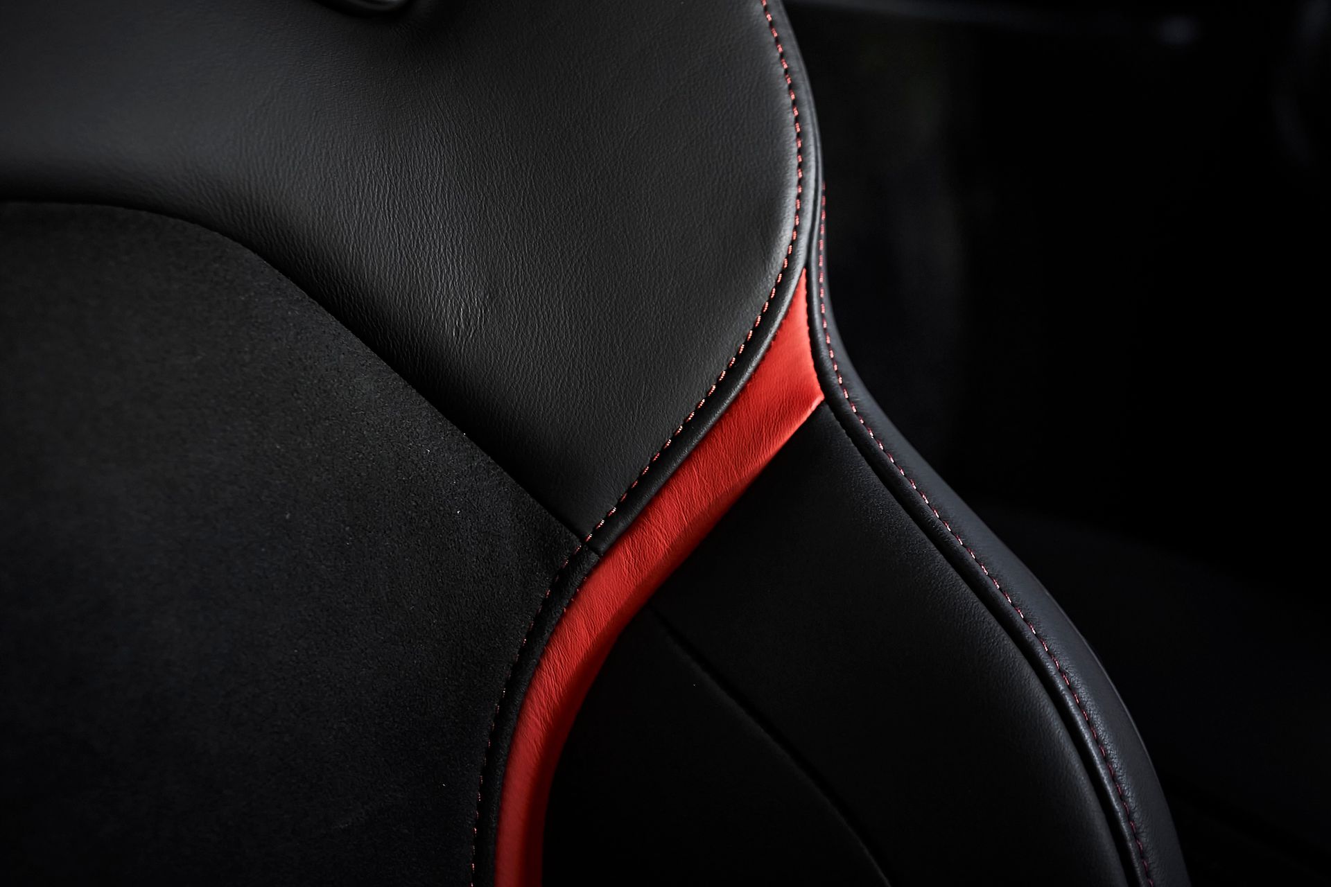A close up of a black leather car seat with a red stitching.
