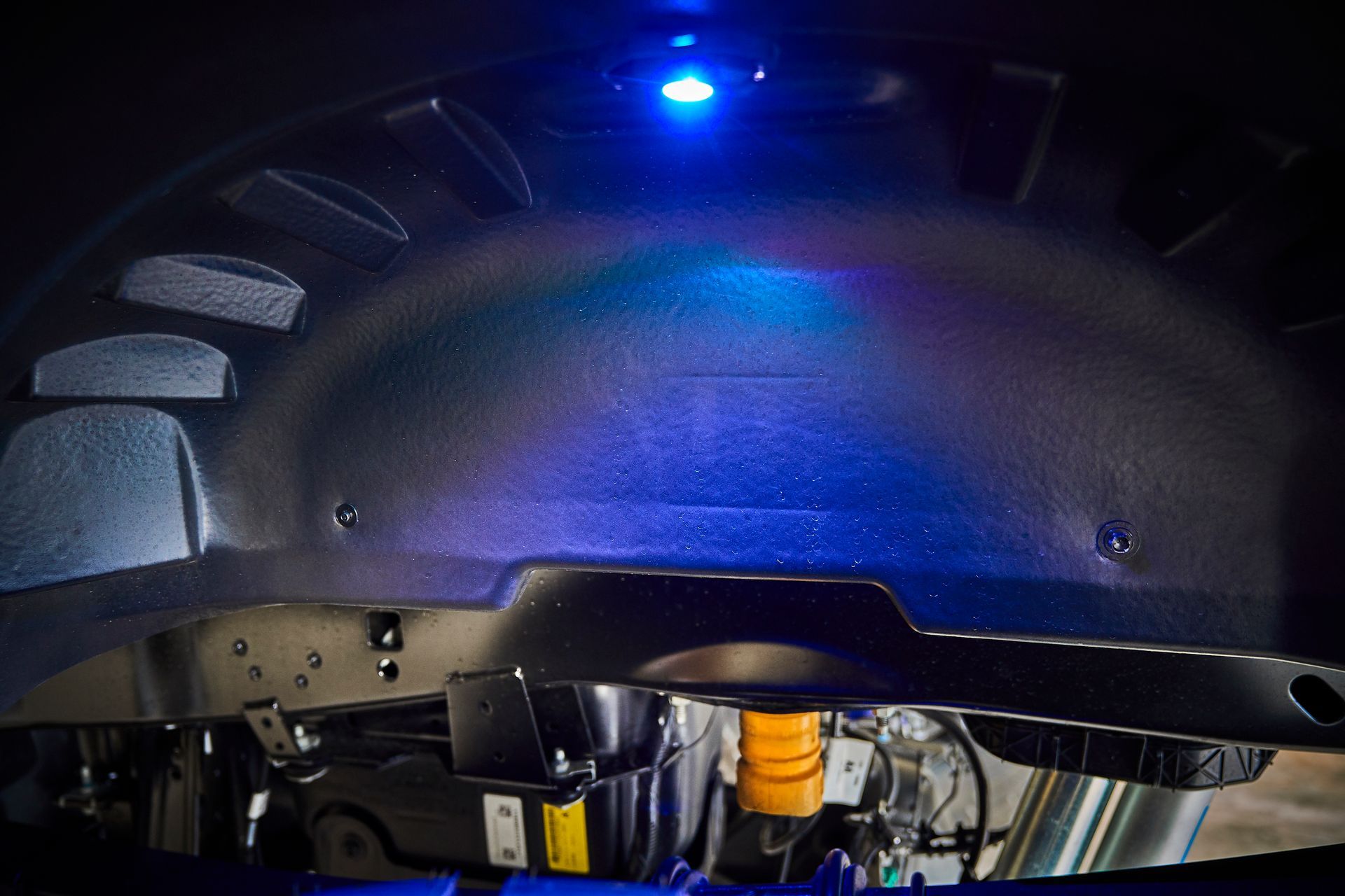 A blue light is shining on the underside of a car.