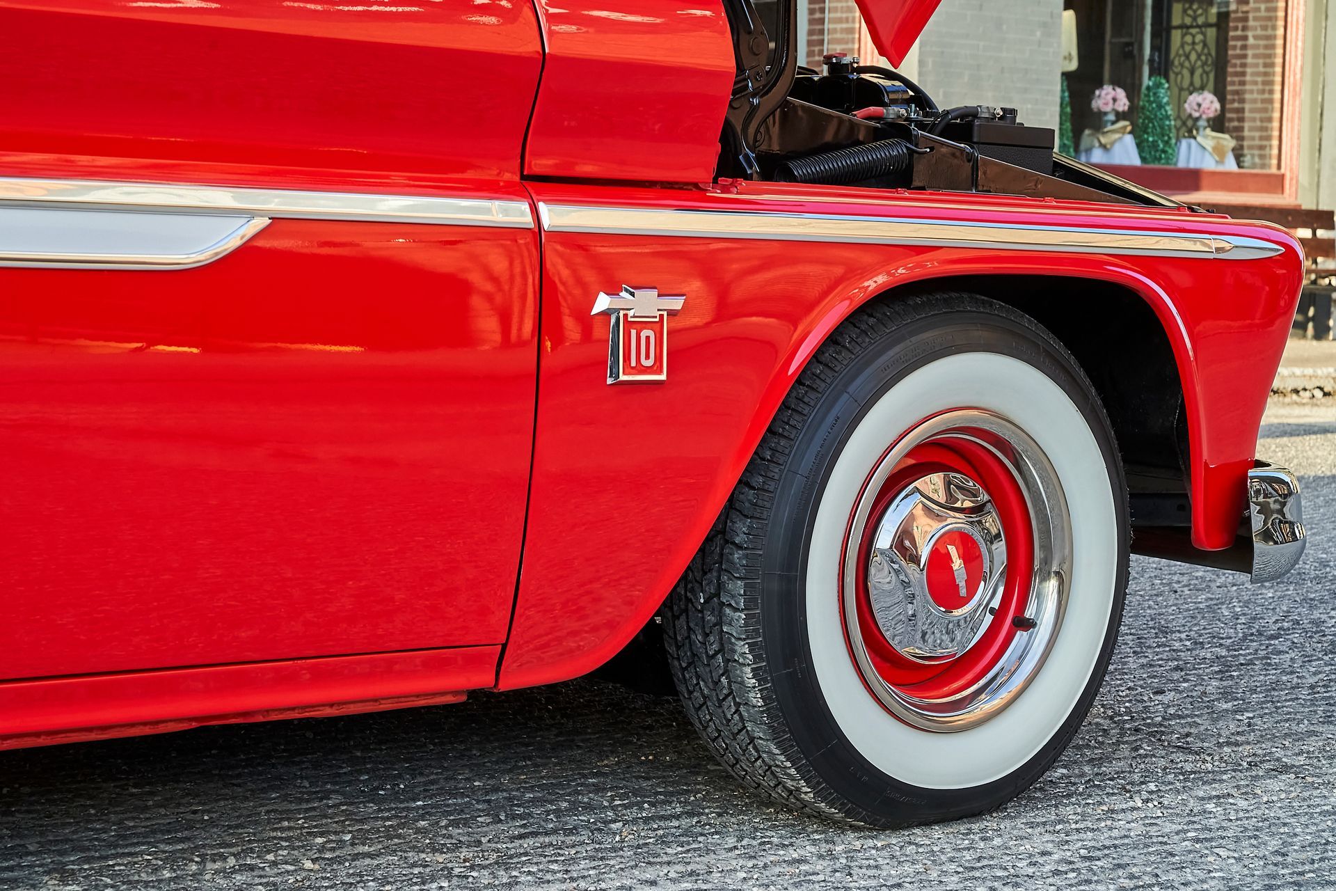 A red truck with the hood up is parked in front of a store