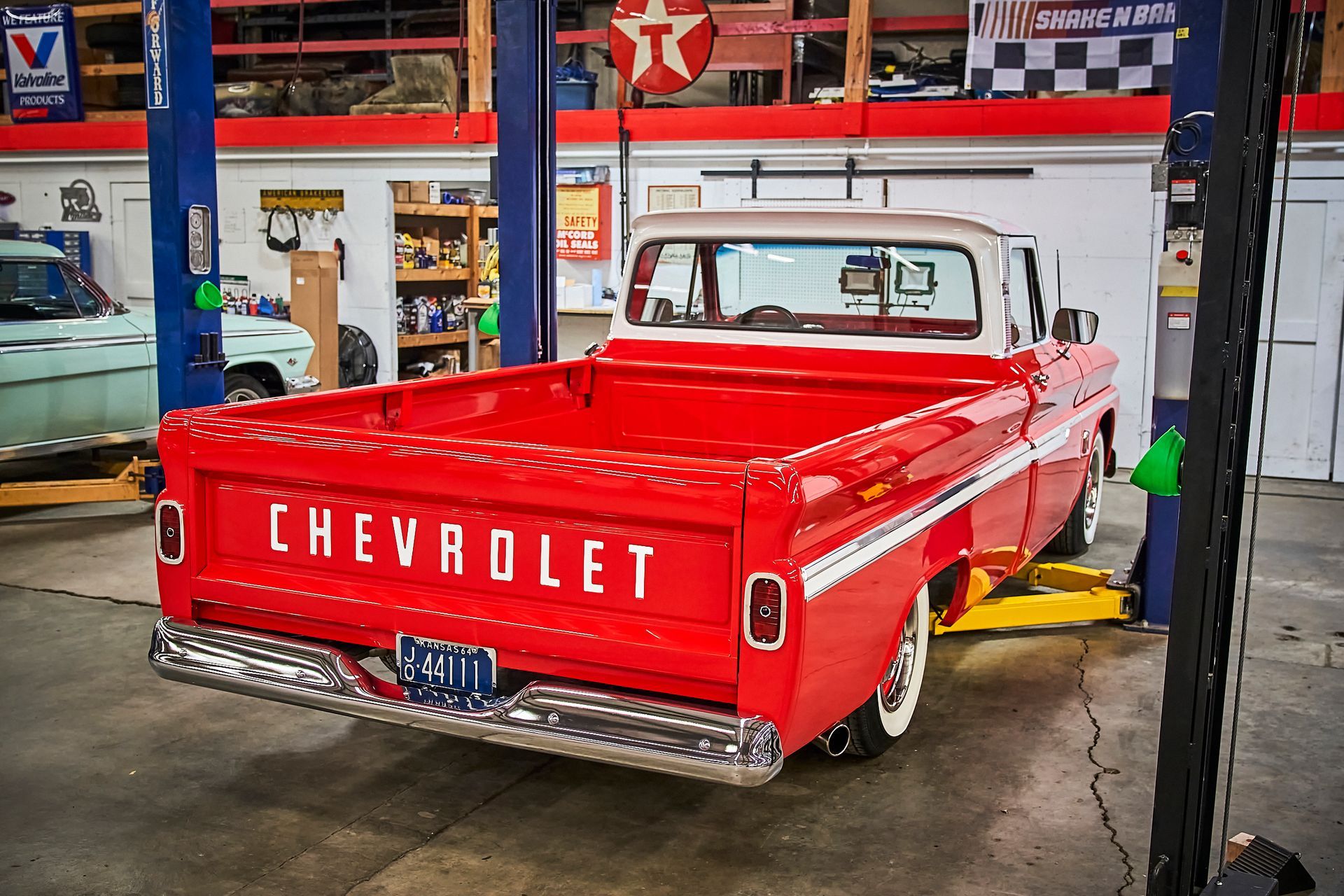 A red chevrolet truck is parked on a lift in a garage.