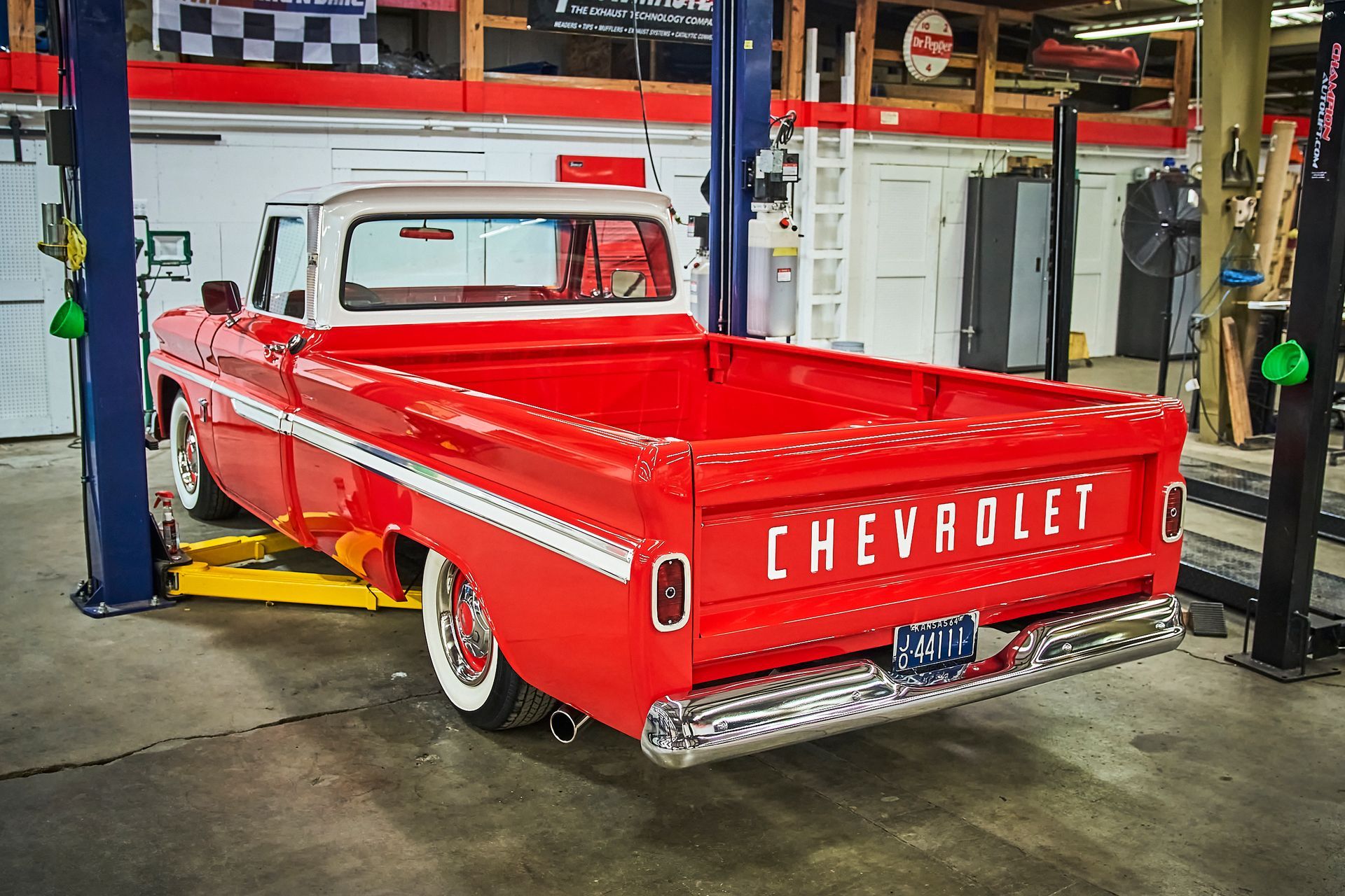 A red chevrolet truck is parked on a lift in a garage.