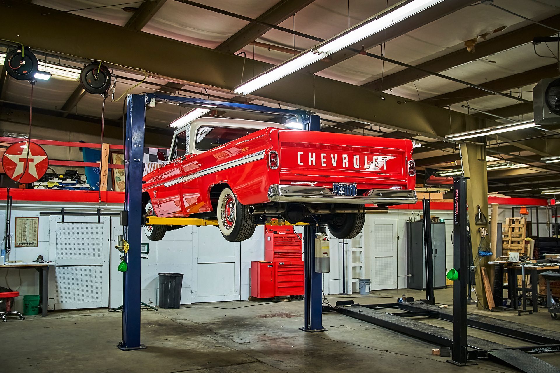 A red chevy truck is on a lift in a garage.