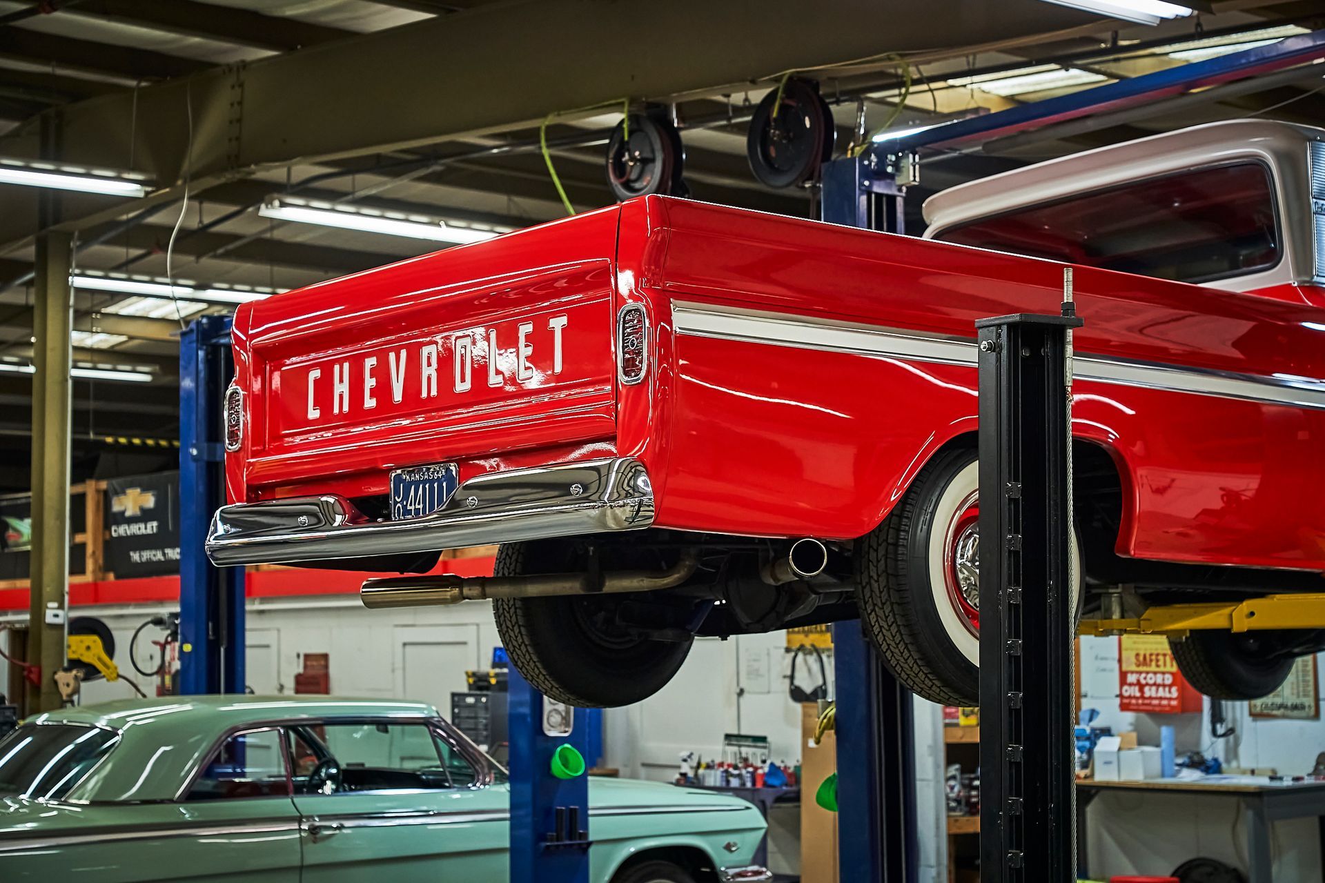 A red chevrolet truck is on a lift in a garage.