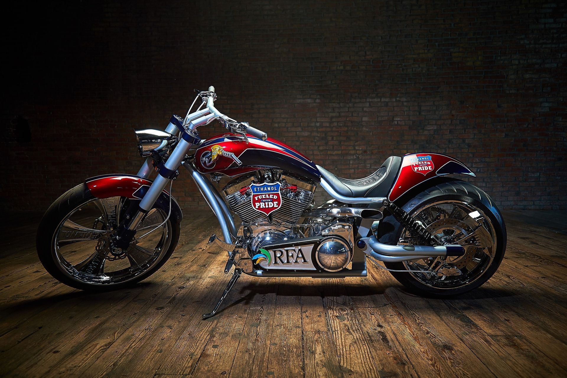 A motorcycle is parked on a wooden floor in front of a brick wall.