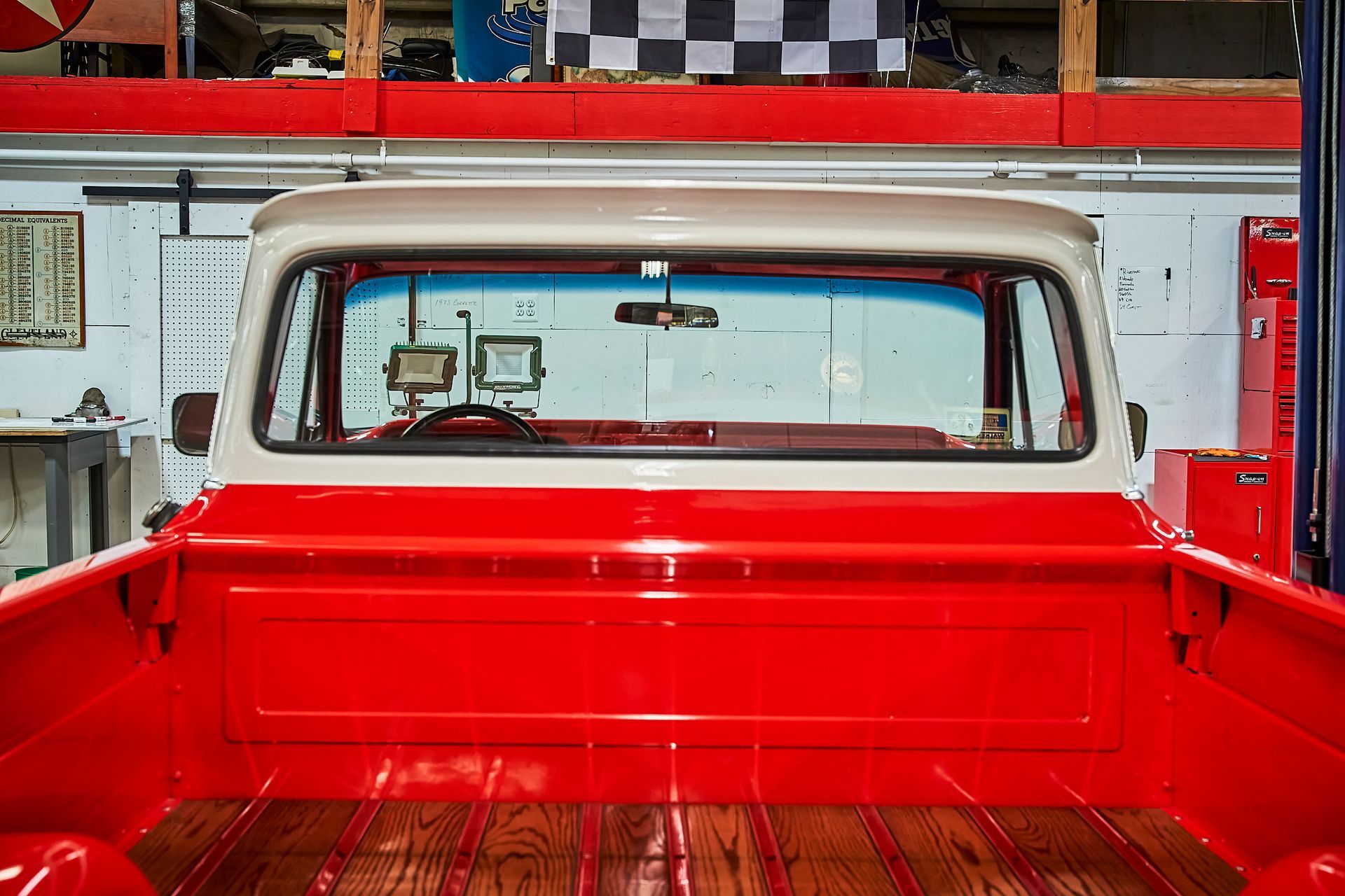 The back of a red truck with a wooden floor in a garage.