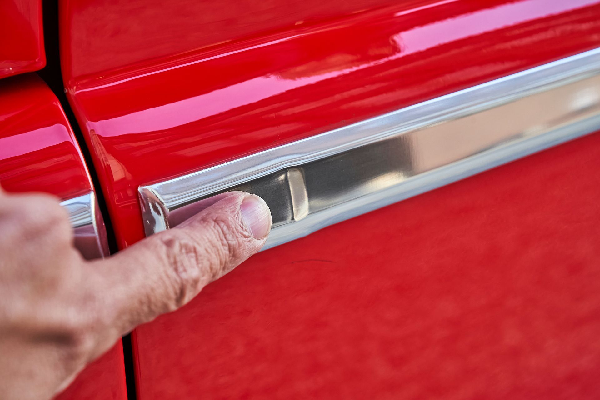 A person is pointing at the door handle of a red car.