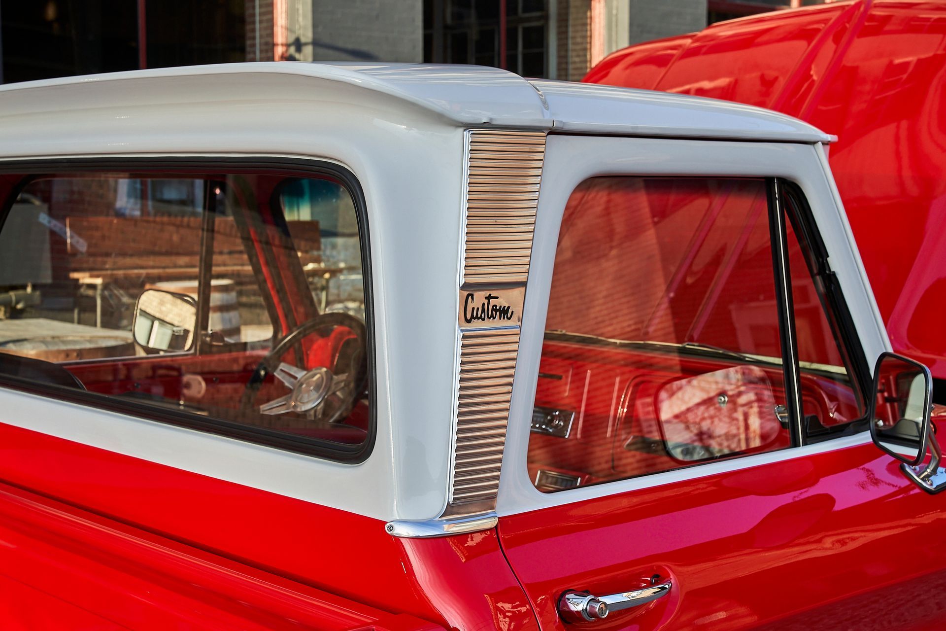 A red truck with a white roof is parked in front of a building.