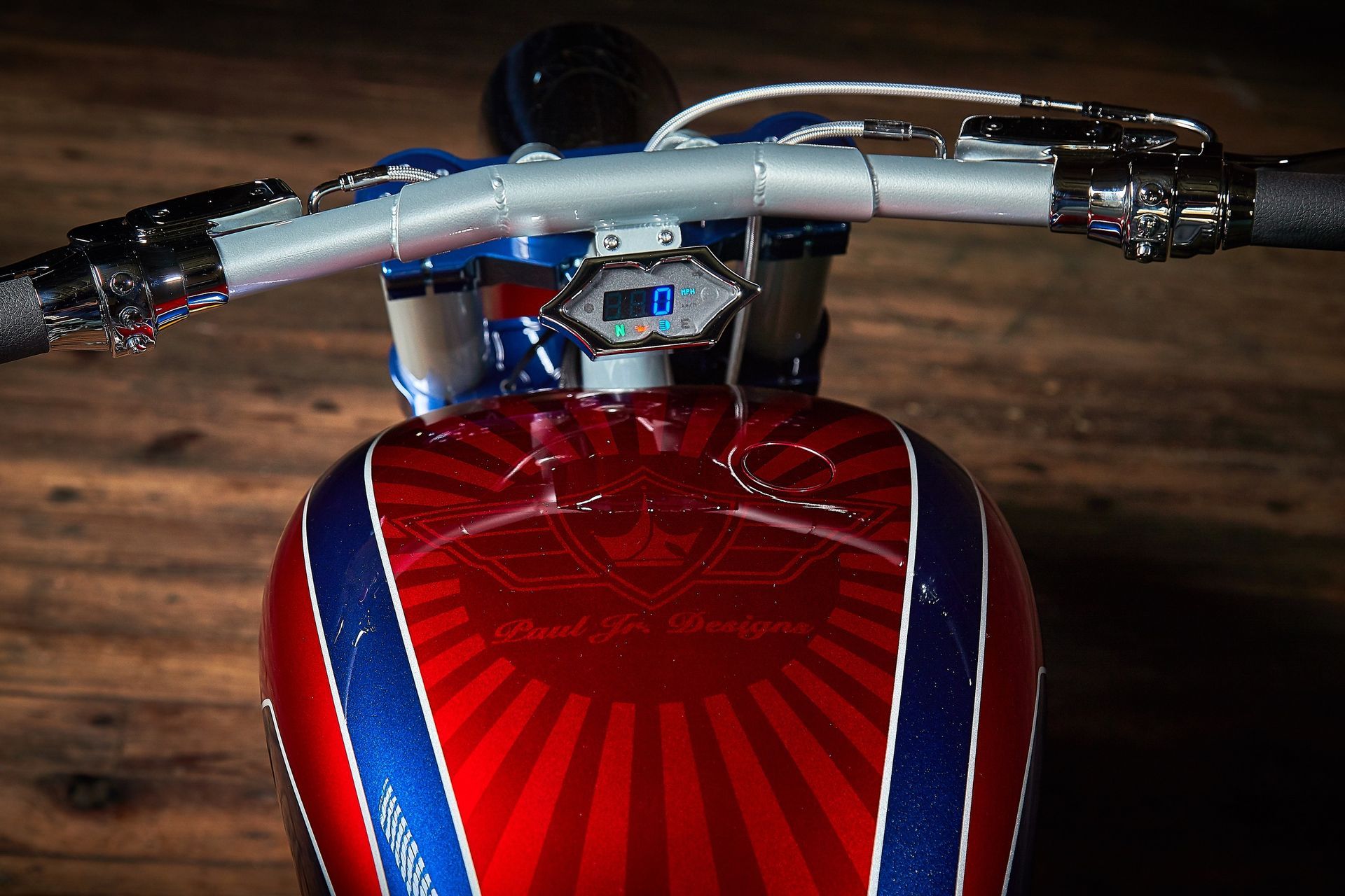 A red , white and blue motorcycle is sitting on a wooden floor