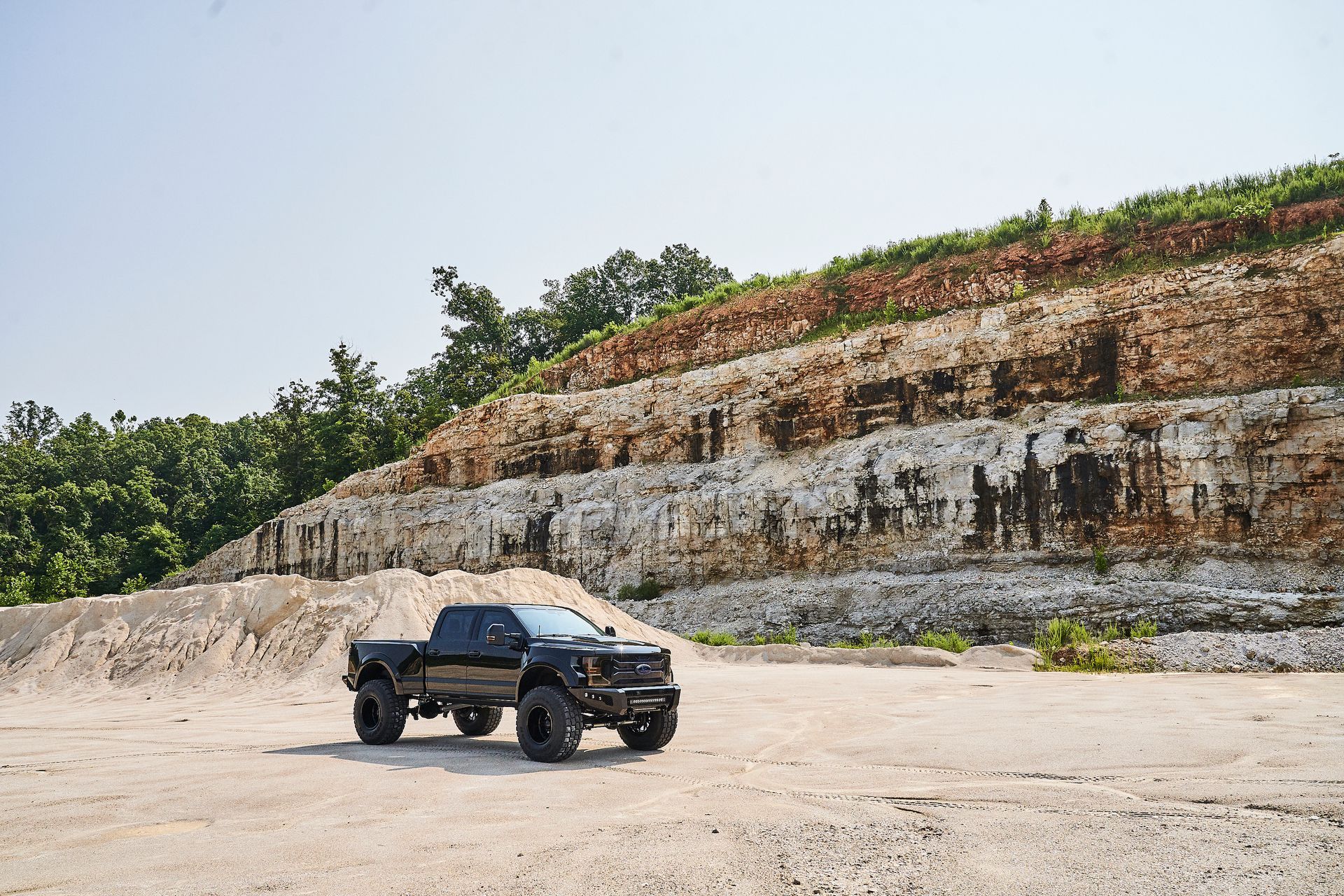 A black truck is parked in a dirt field in front of a large rock formation.