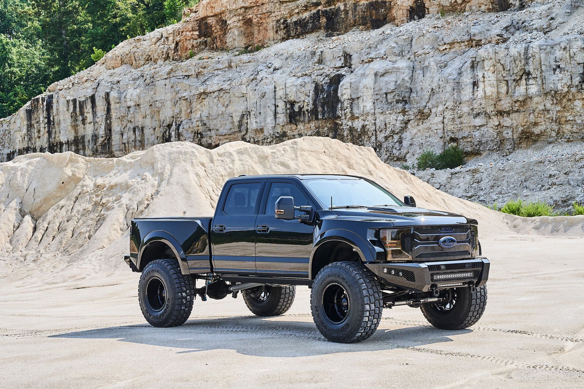 A black truck is parked in a dirt field in front of a pile of rocks.