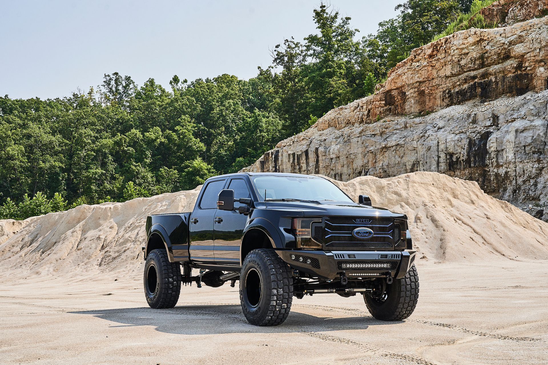 A black truck is parked in a dirt field in front of a pile of dirt.