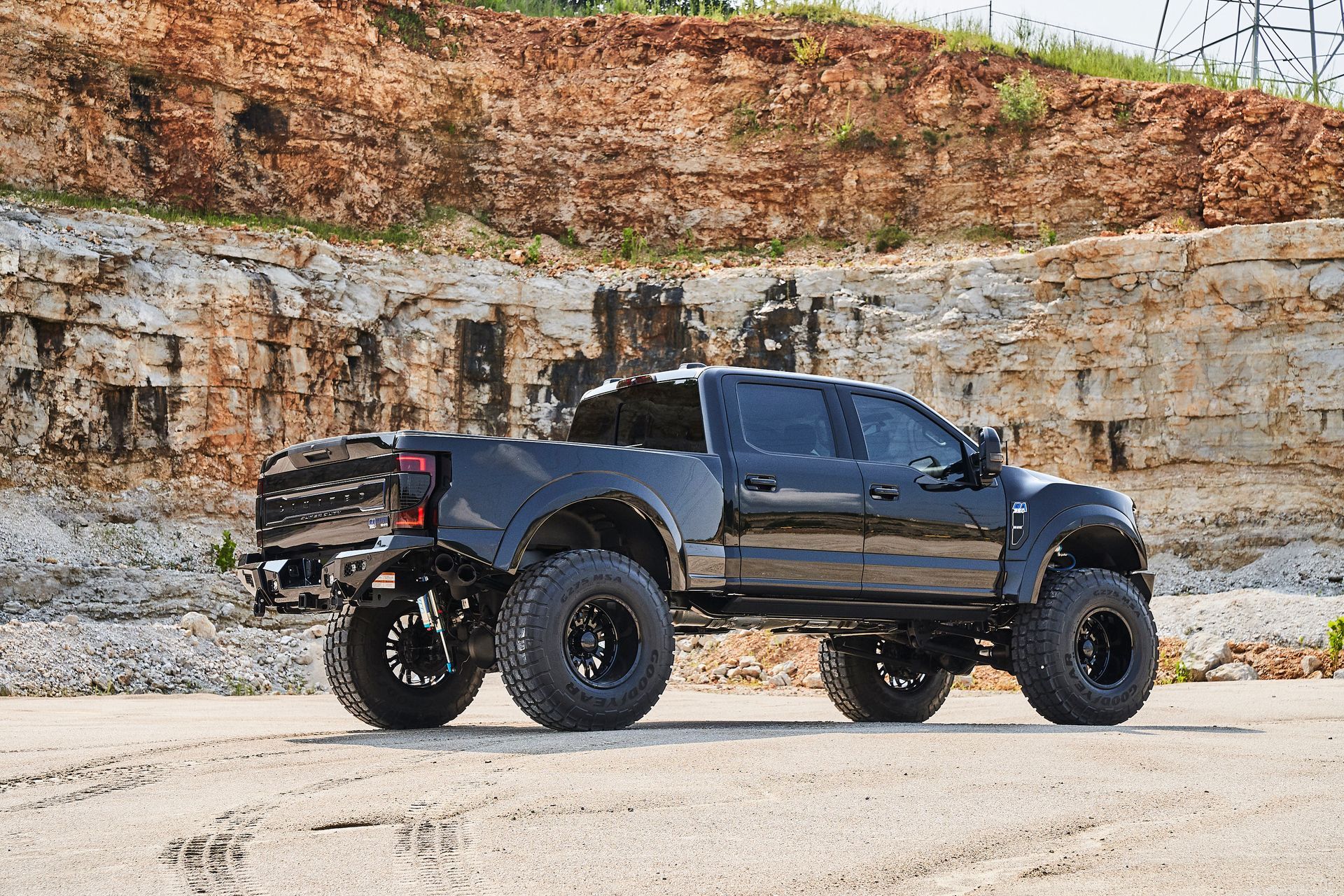A black truck is parked on the side of the road in front of a rocky hill.