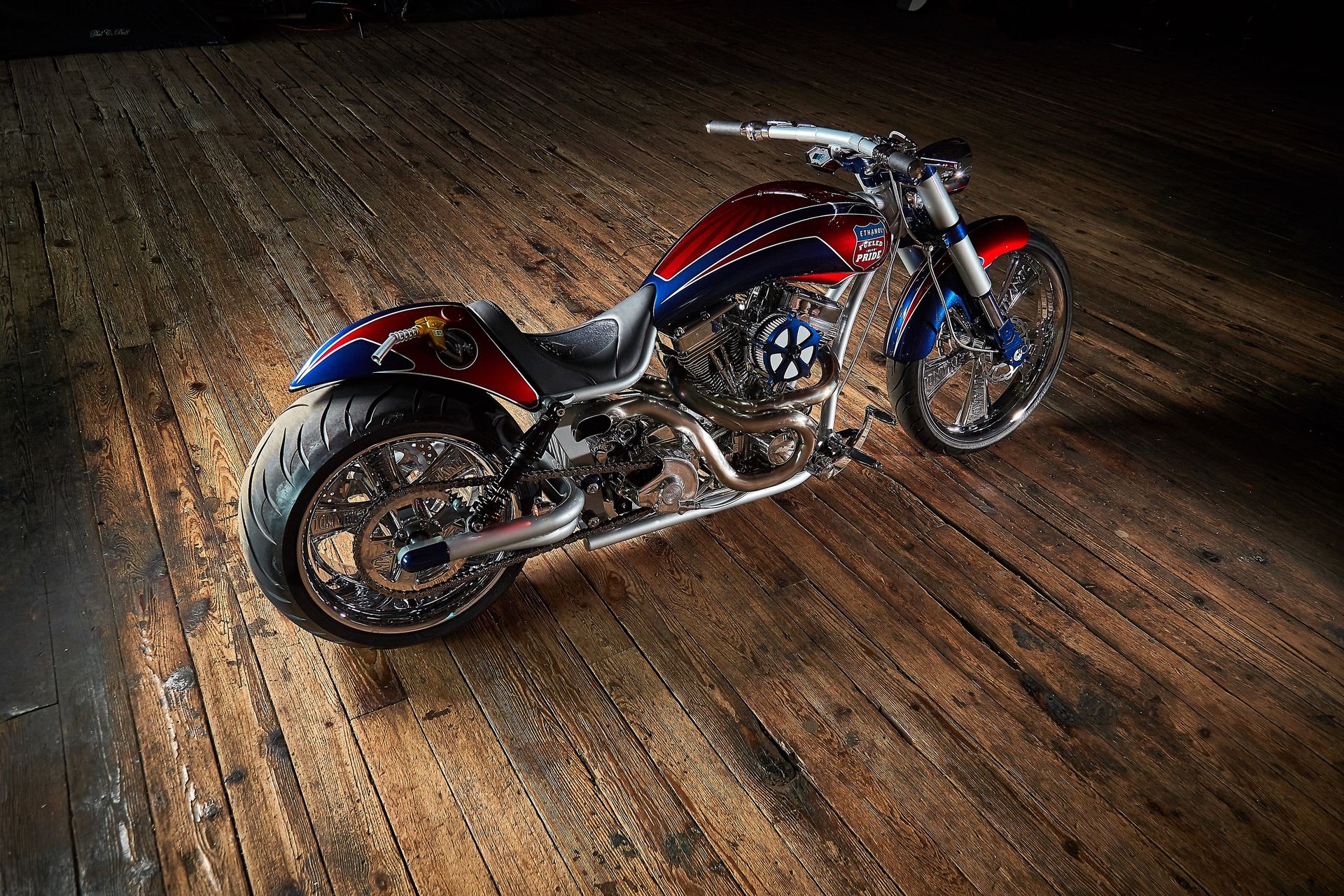 A red , white and blue motorcycle is parked on a wooden floor.