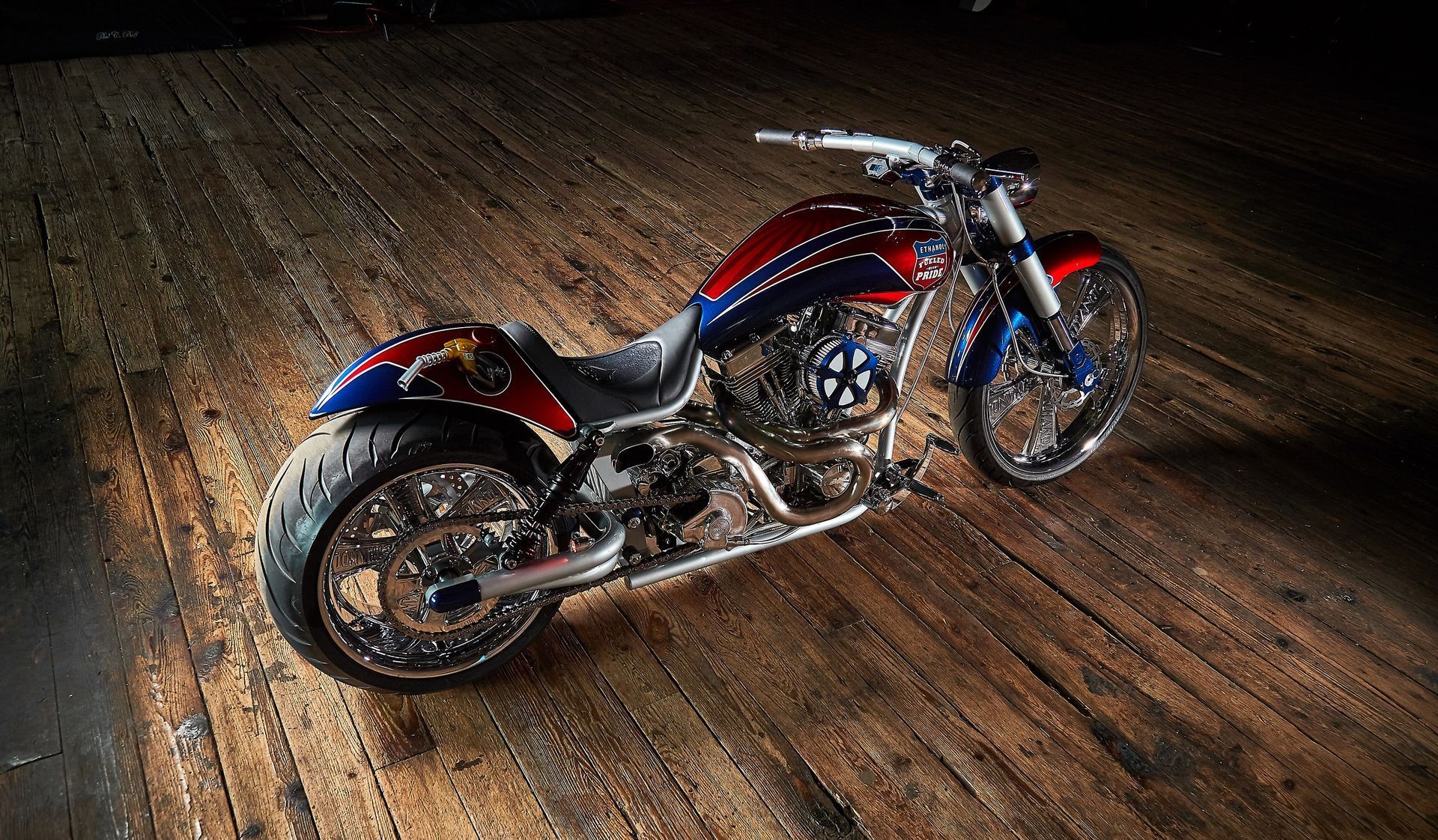 A red , white and blue motorcycle is parked on a wooden floor.