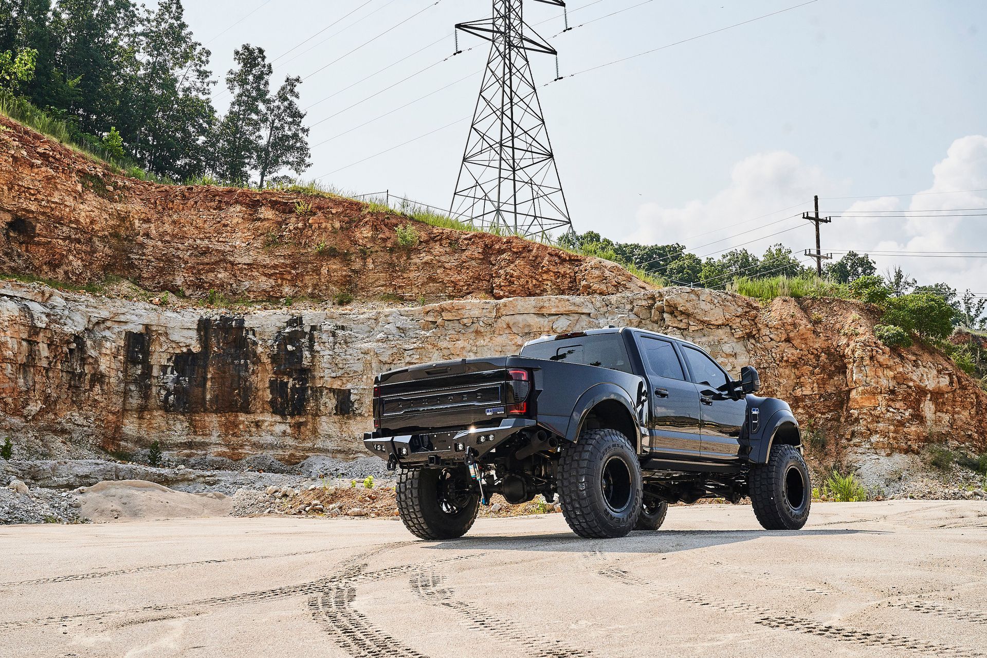 A black truck is parked on the side of a dirt road next to a mountain.