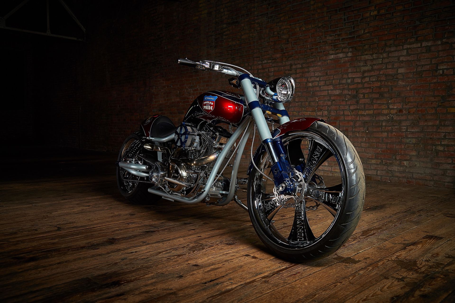 A motorcycle is parked in front of a brick wall in a dark room.