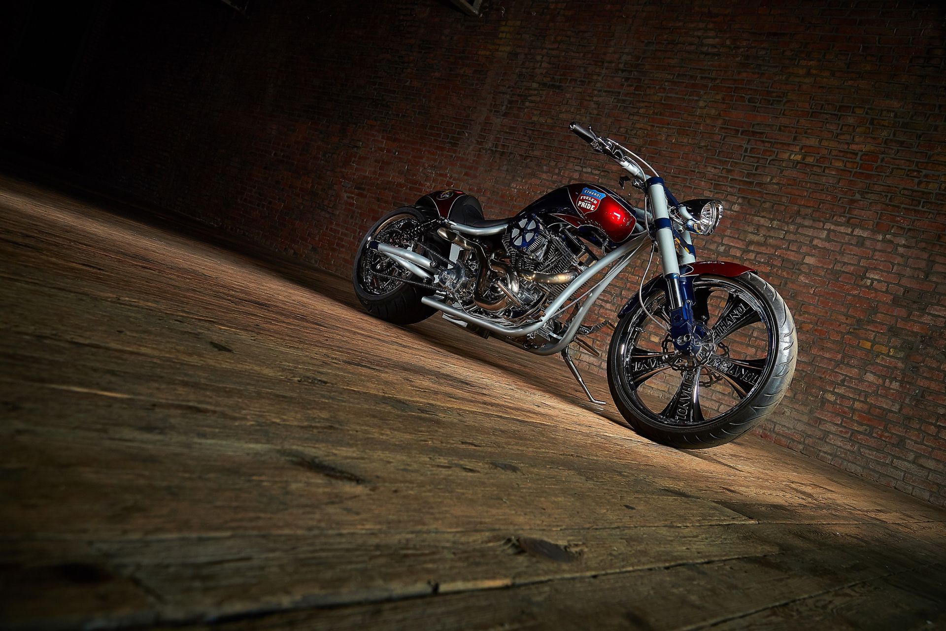 A motorcycle is parked on a wooden floor in front of a brick wall.