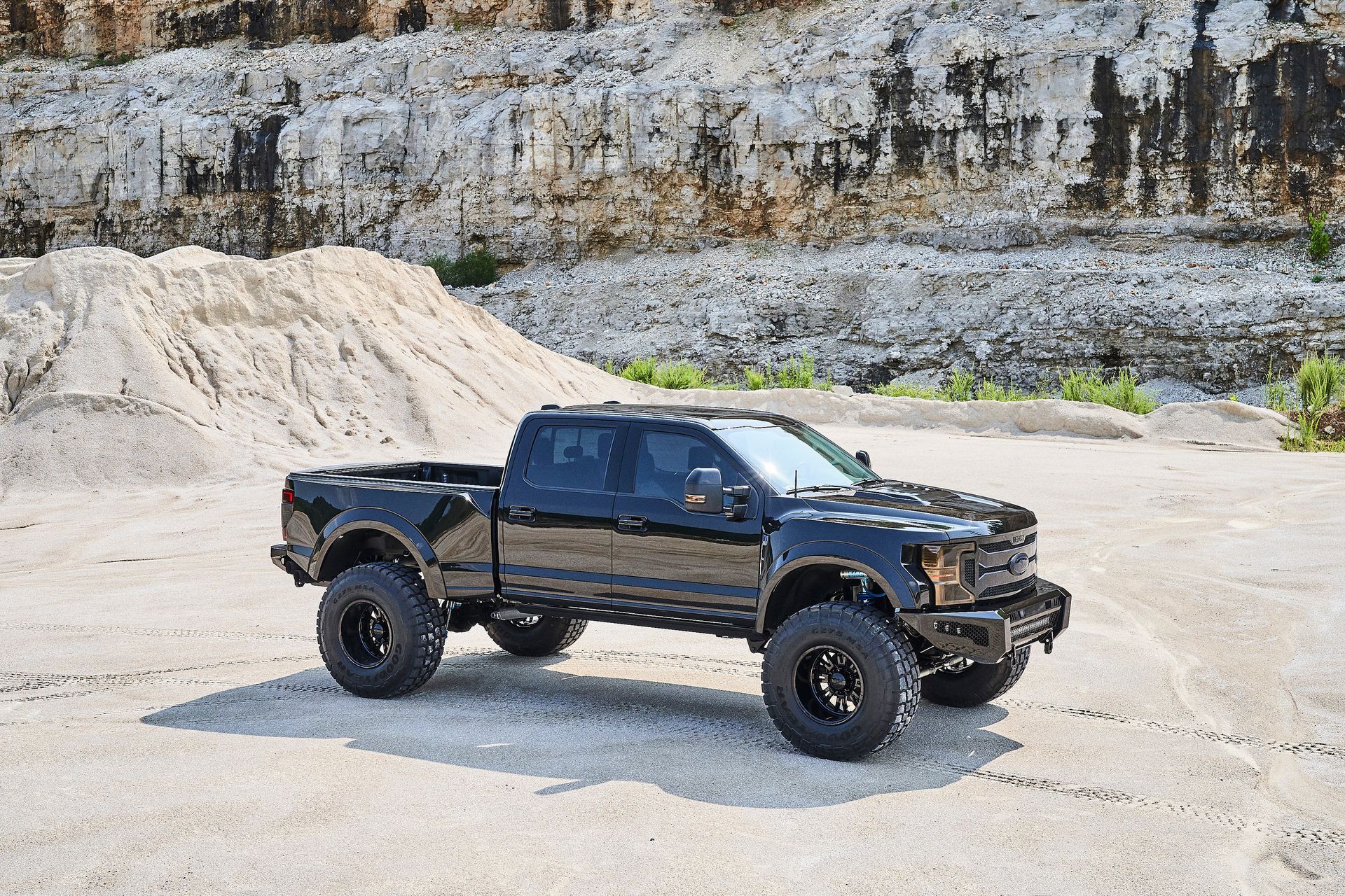 A black truck is parked in a dirt field in front of a large rock formation.