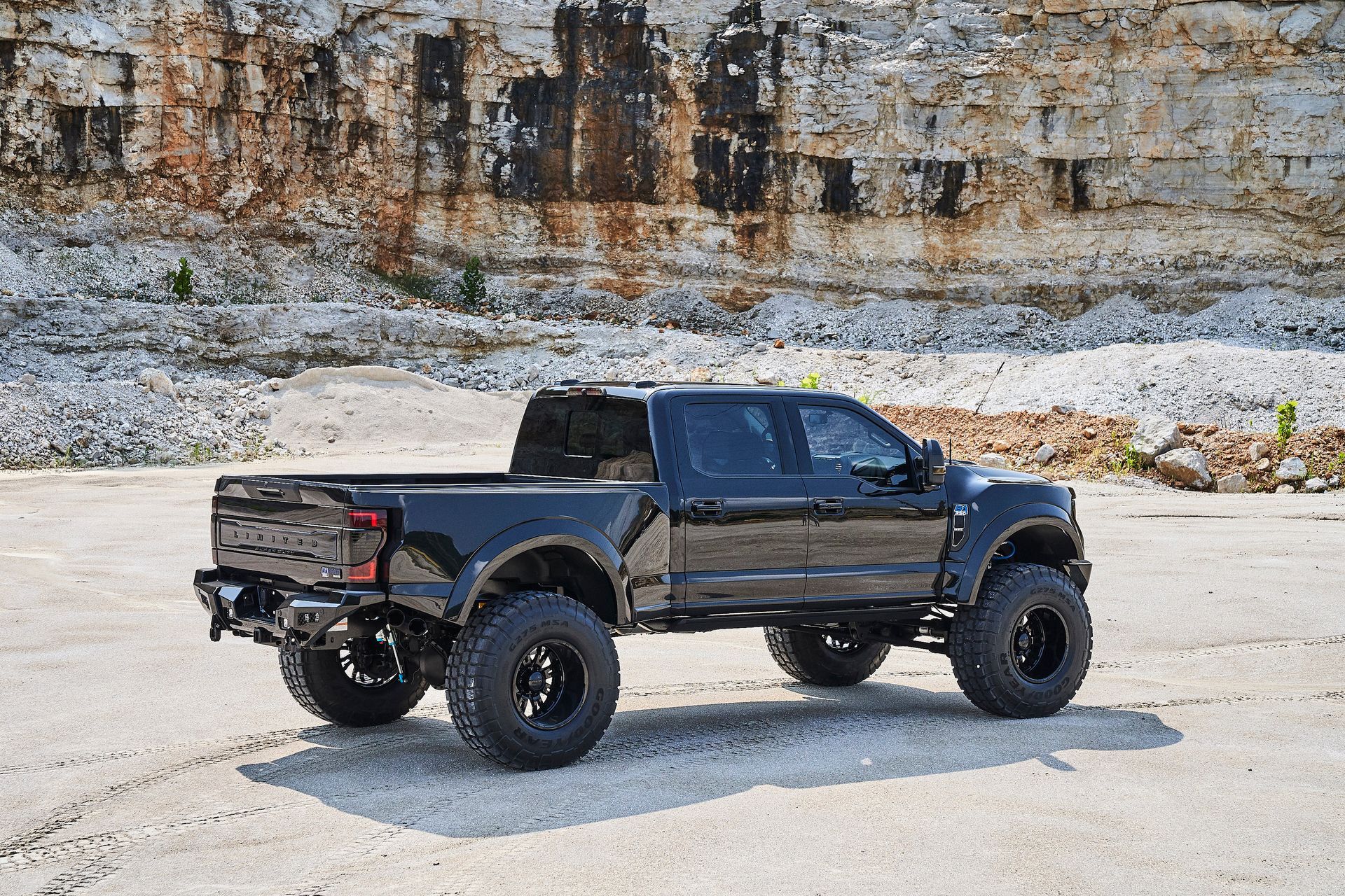 A black truck is parked on the side of the road in front of a rock wall.
