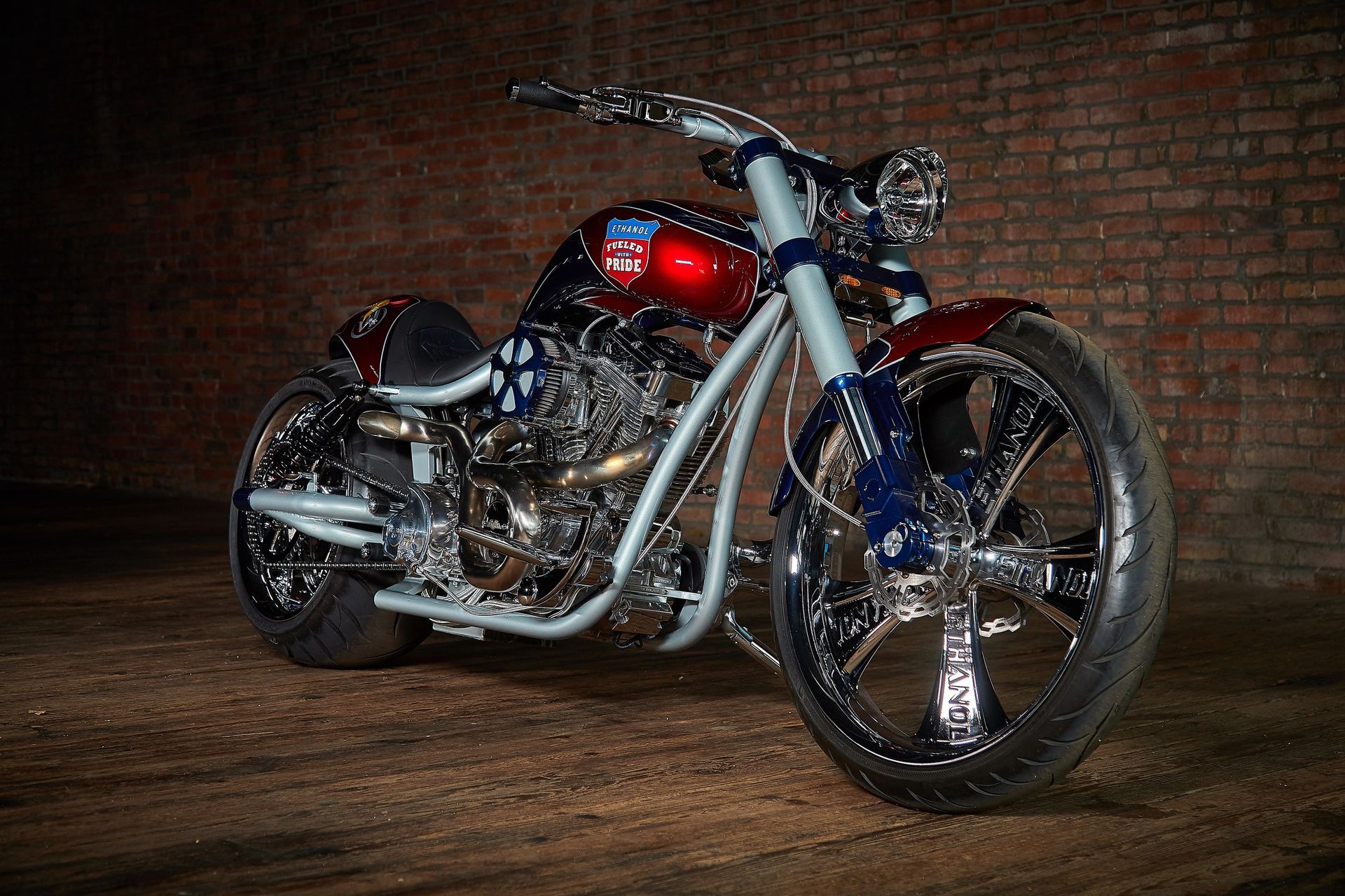 A red , white and blue motorcycle is parked in front of a brick wall.