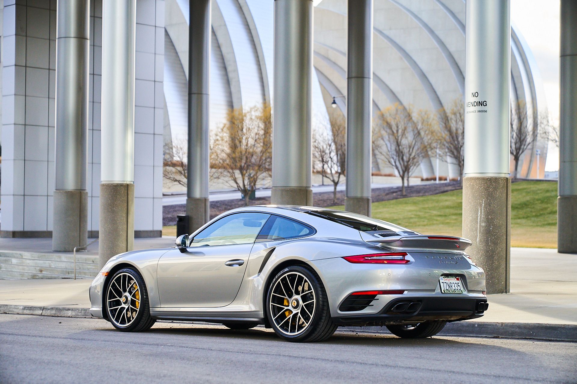 A silver porsche 911 turbo s is parked on the side of the road in front of a building.