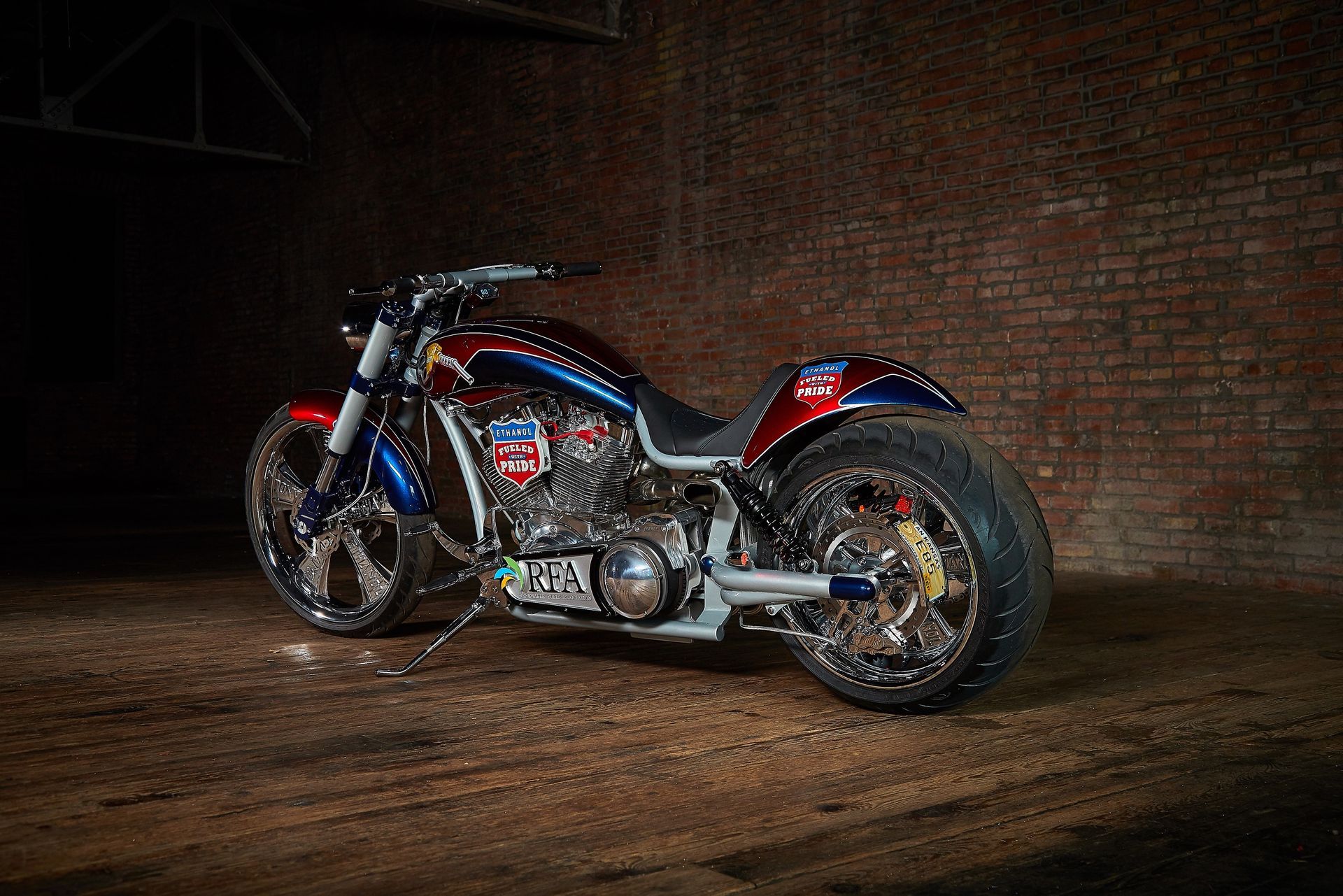 A red , white and blue motorcycle is parked in front of a brick wall.