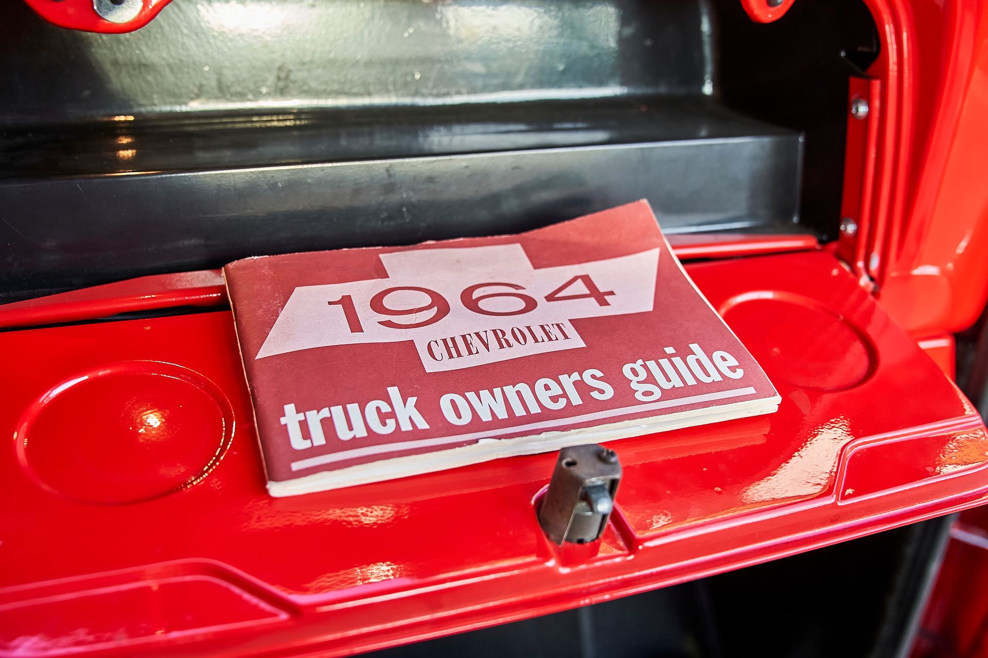 A 1964 chevrolet truck owners guide is sitting in the trunk of a red truck.