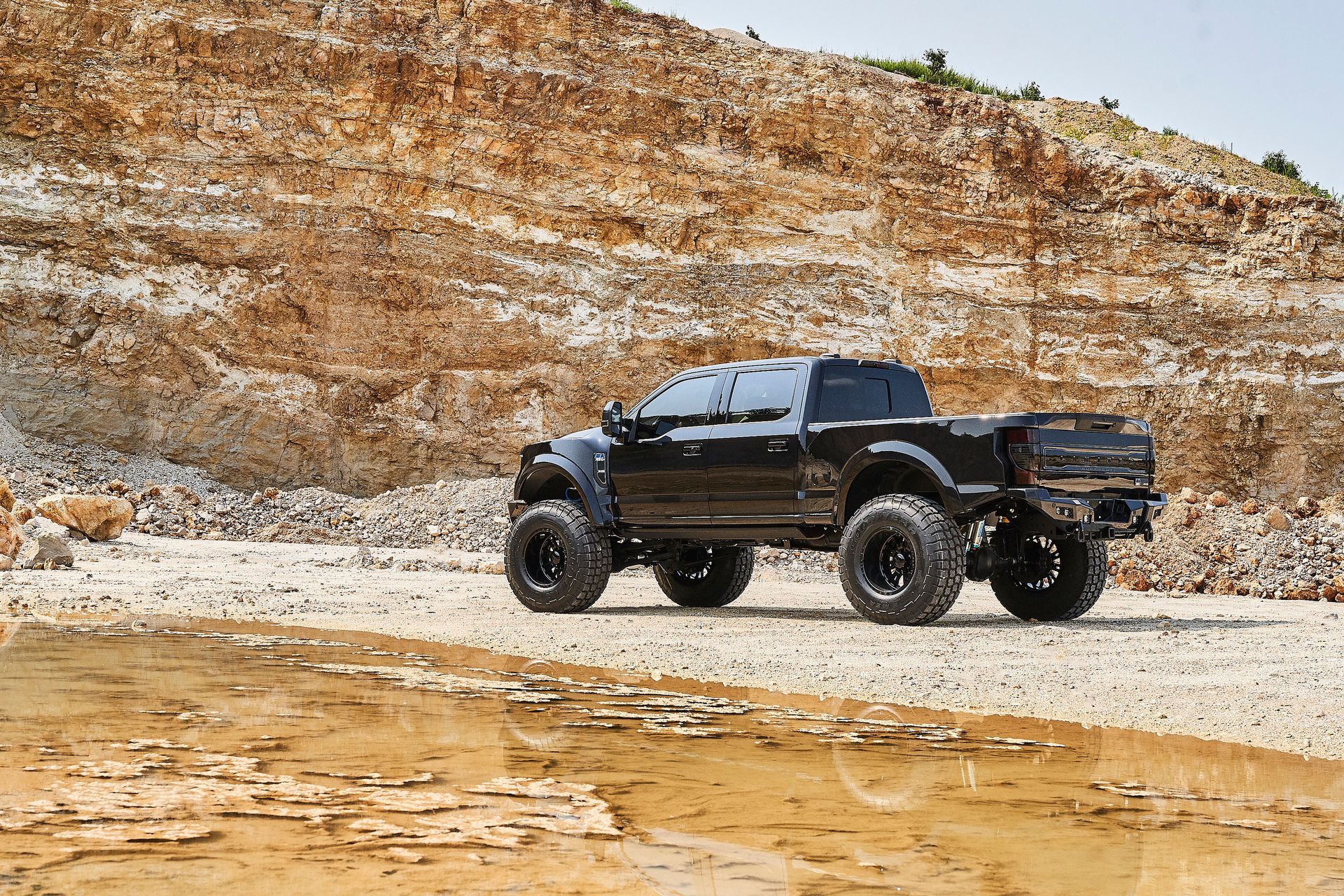A black truck is parked on a dirt road in front of a mountain.