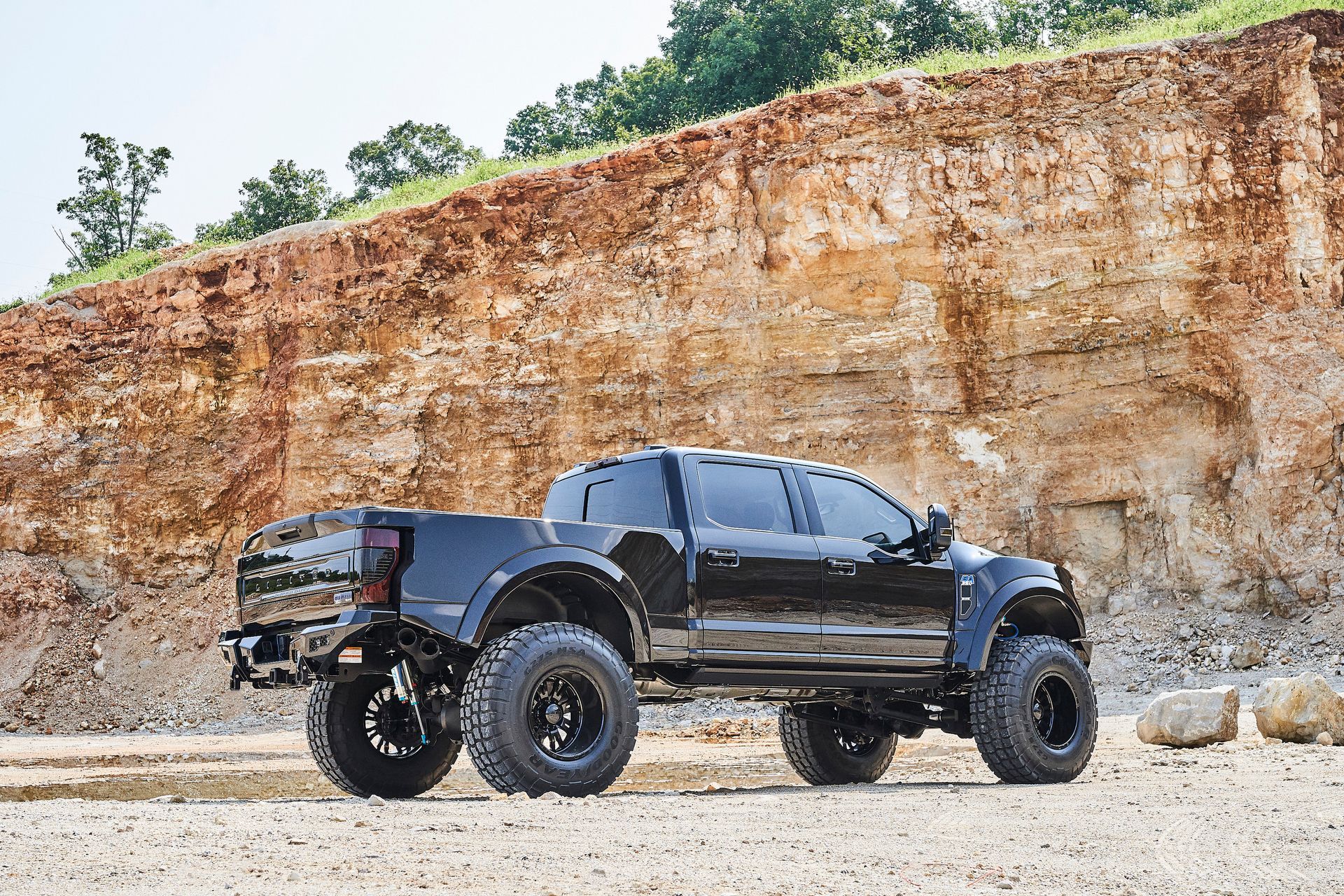 A black truck is parked in front of a large rock formation.