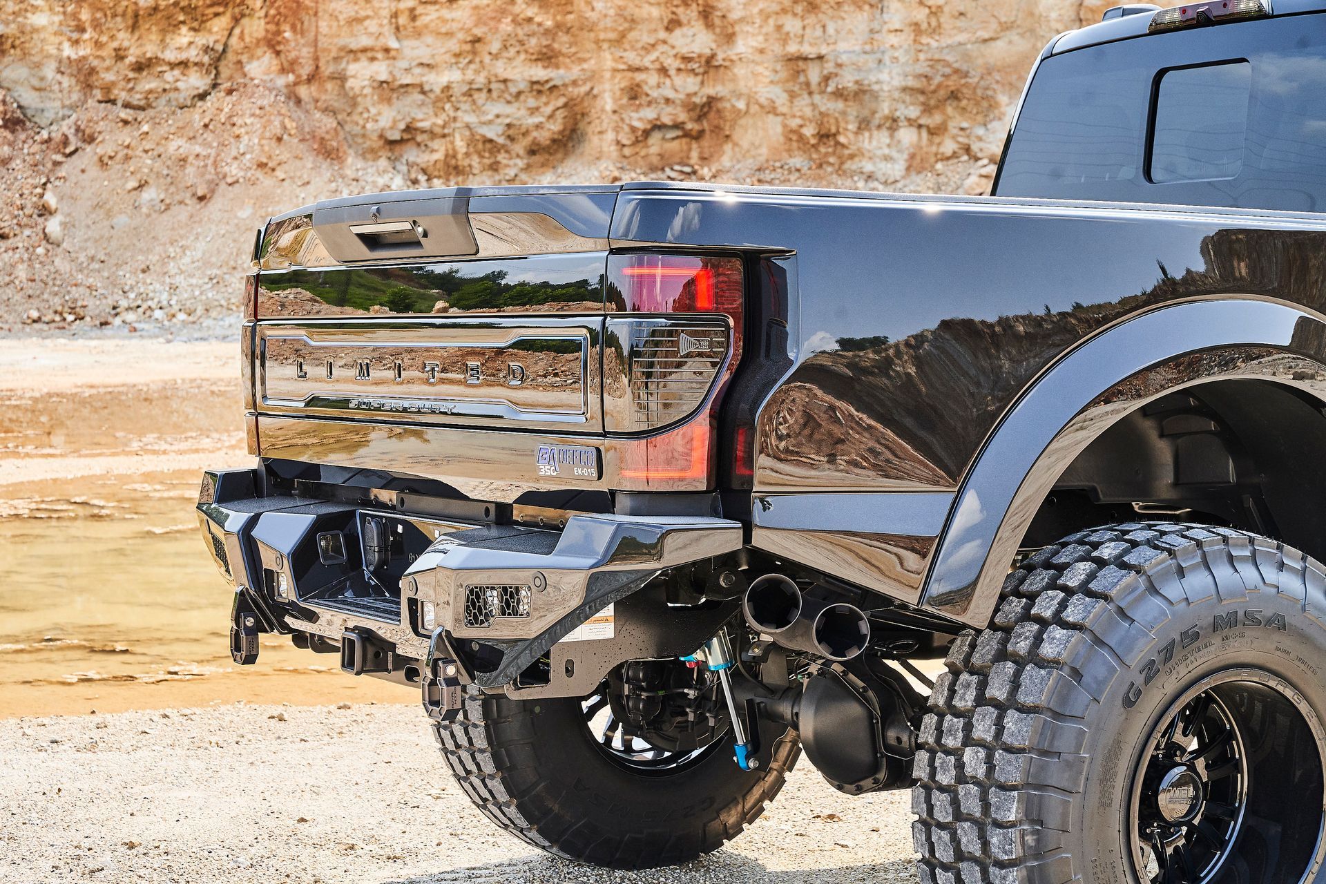 A black truck with a rear bumper is parked on a gravel road.