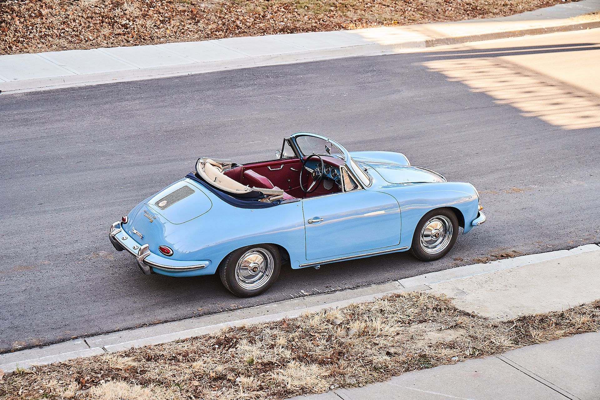 A blue porsche convertible is driving down a street.