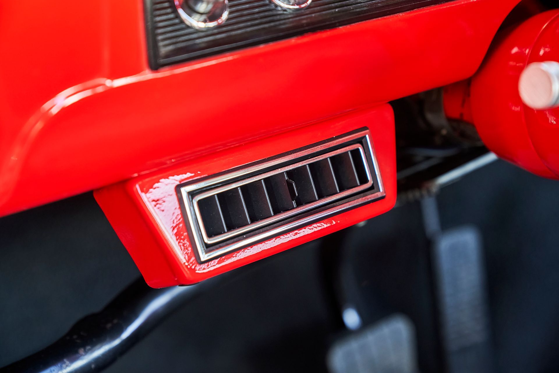 A close up of a red car dashboard with a steering wheel and a brake pedal.