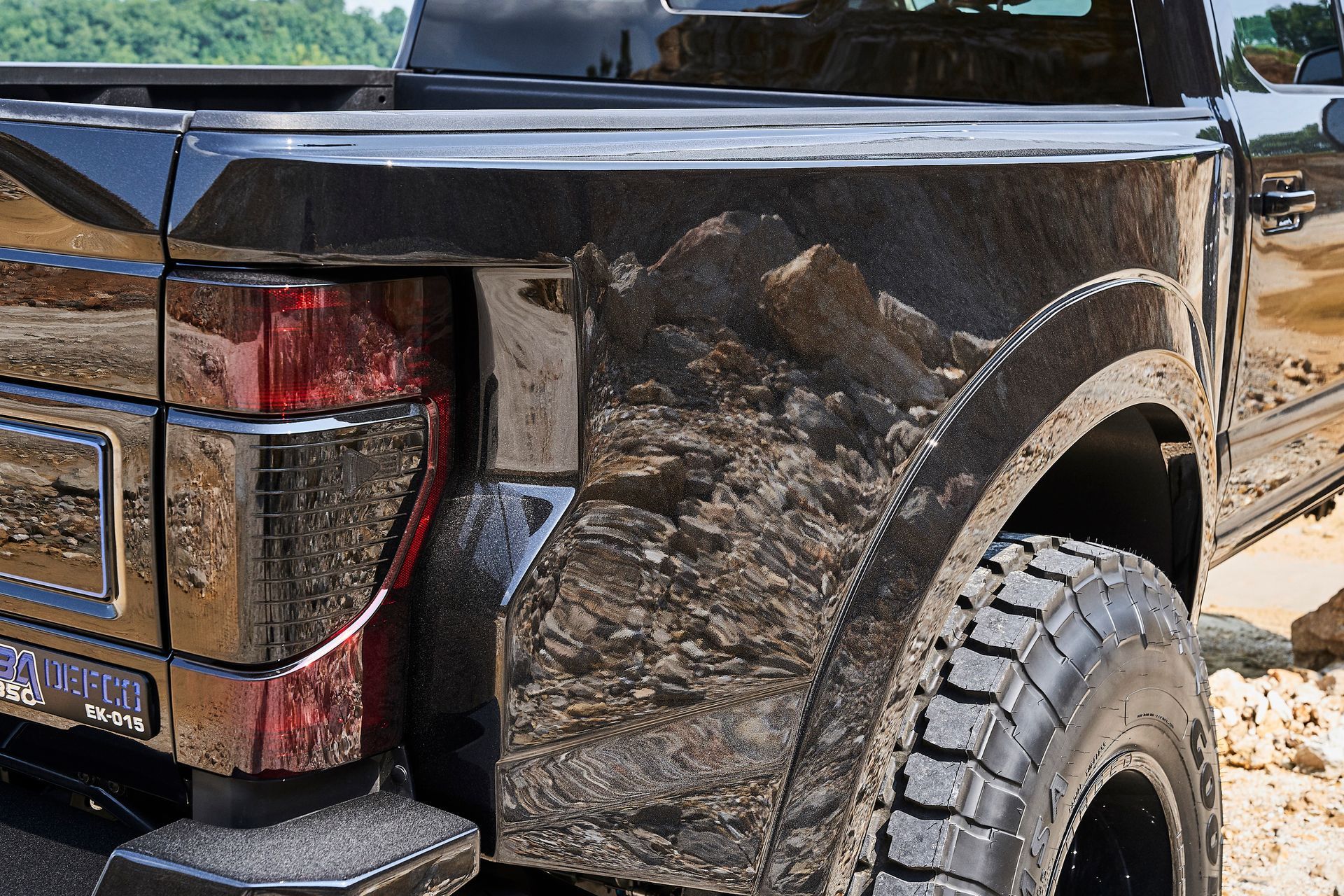 The back of a black truck is covered in mud.