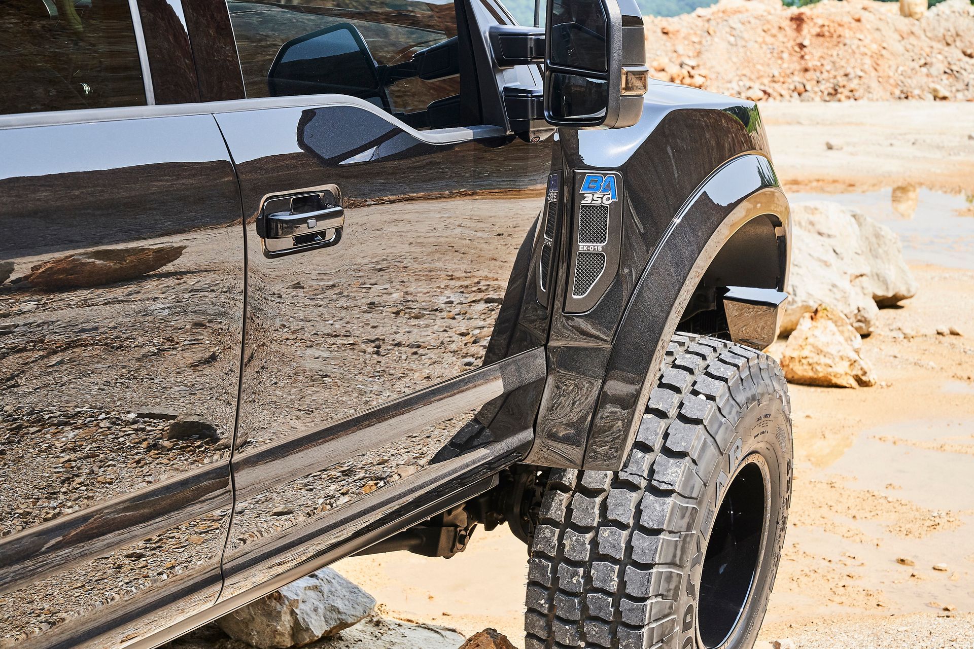 A black truck with big tires is parked in the dirt.