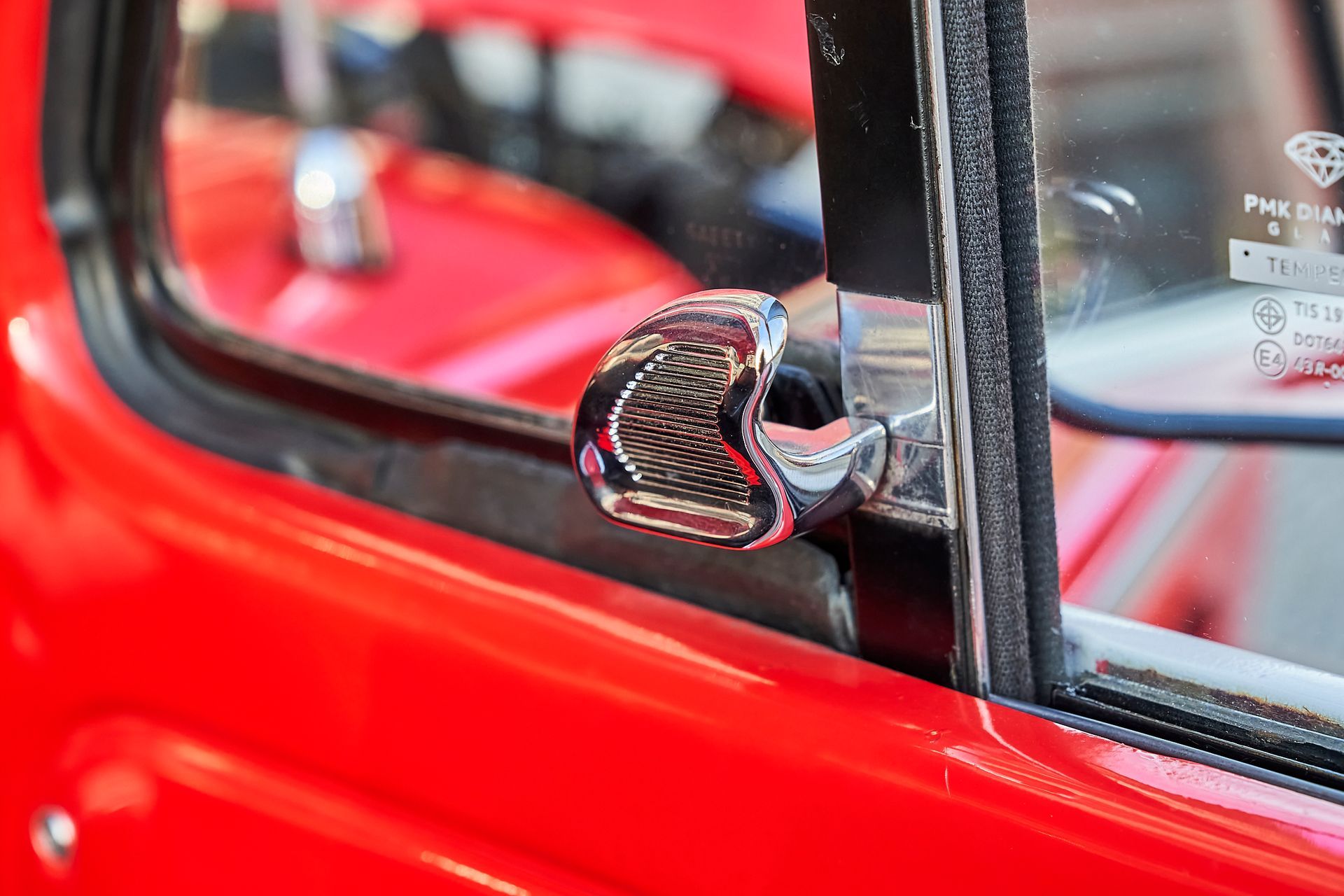 A close up of a red car window with a chrome handle.
