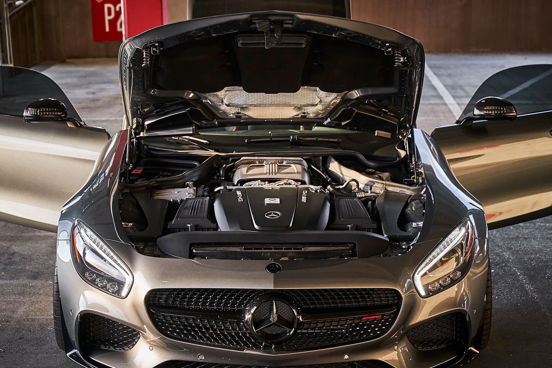 A mercedes with its hood open is parked in a parking garage.