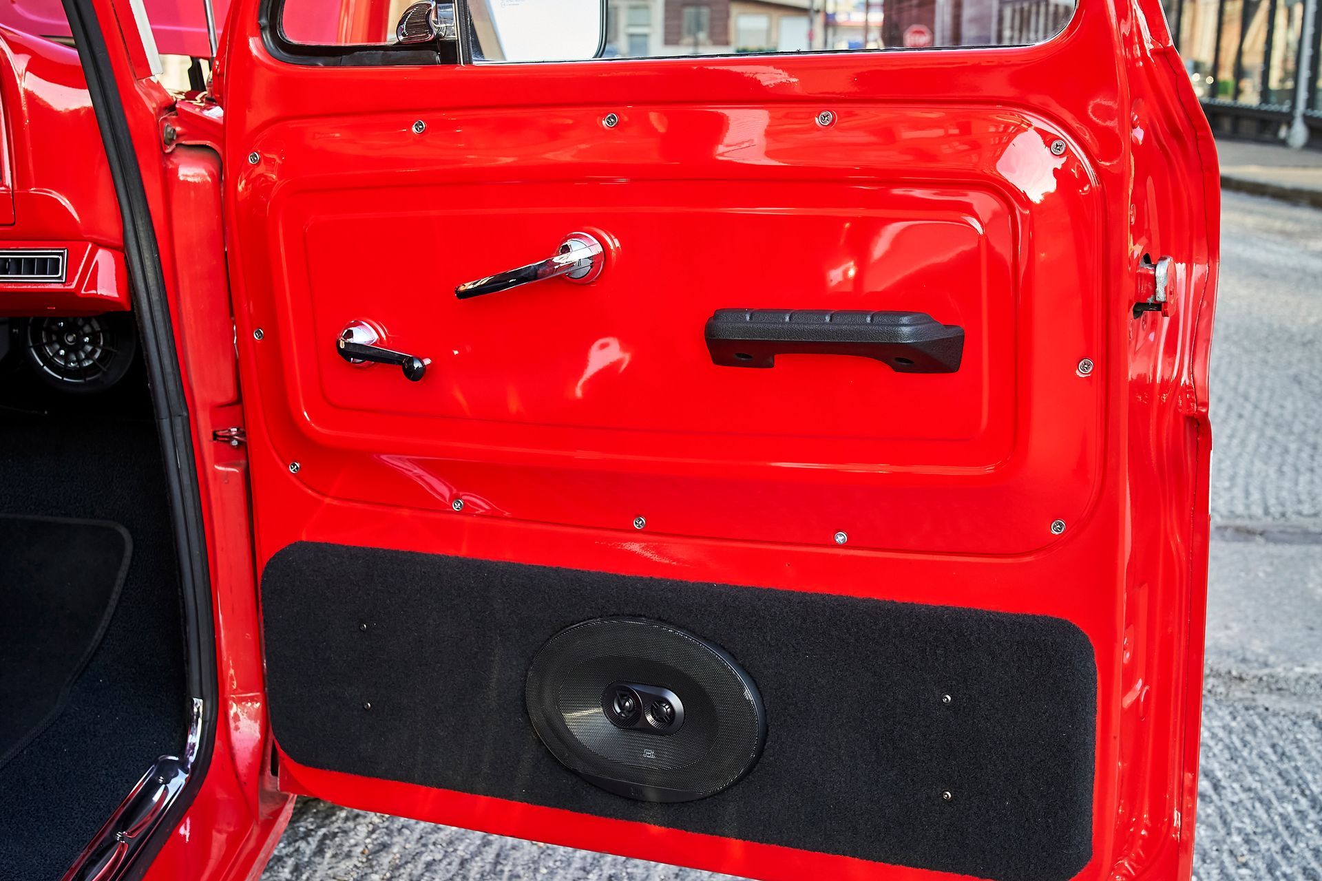 The door of a red truck with a speaker in the back.
