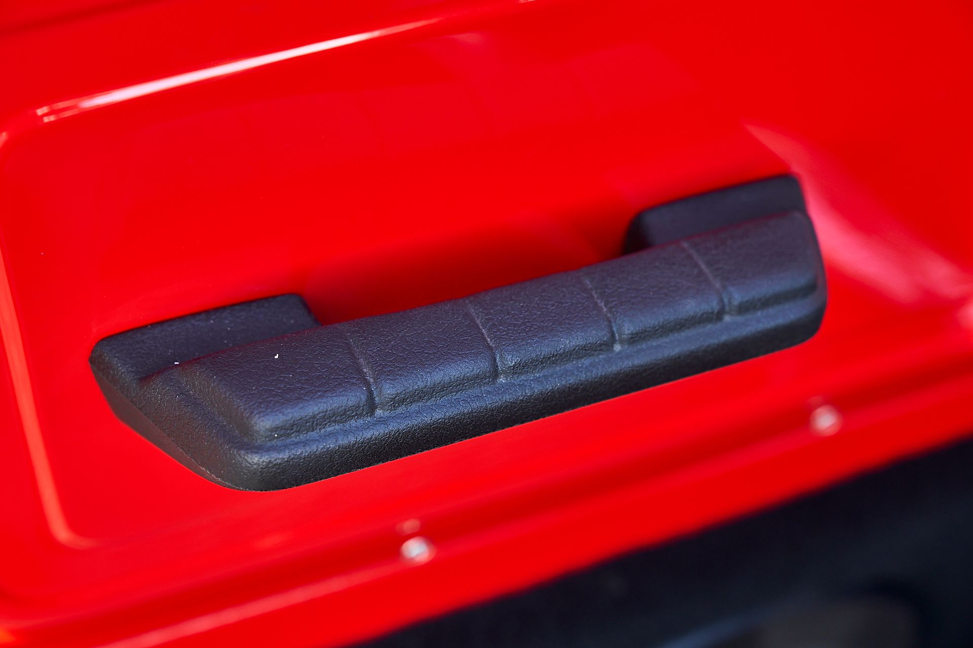 A close up of a black door handle on a red car.