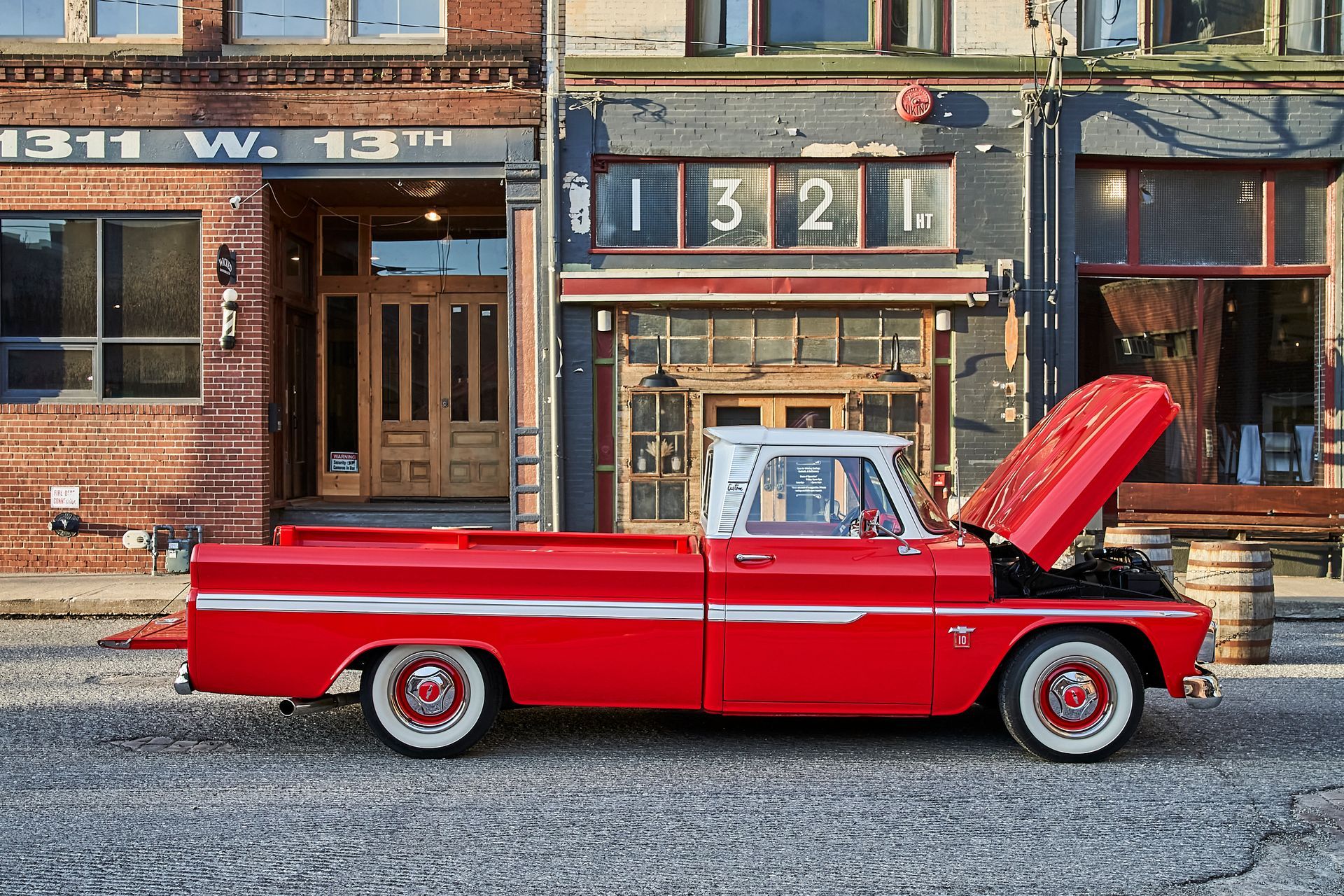 A red truck is parked in front of a building with the hood open